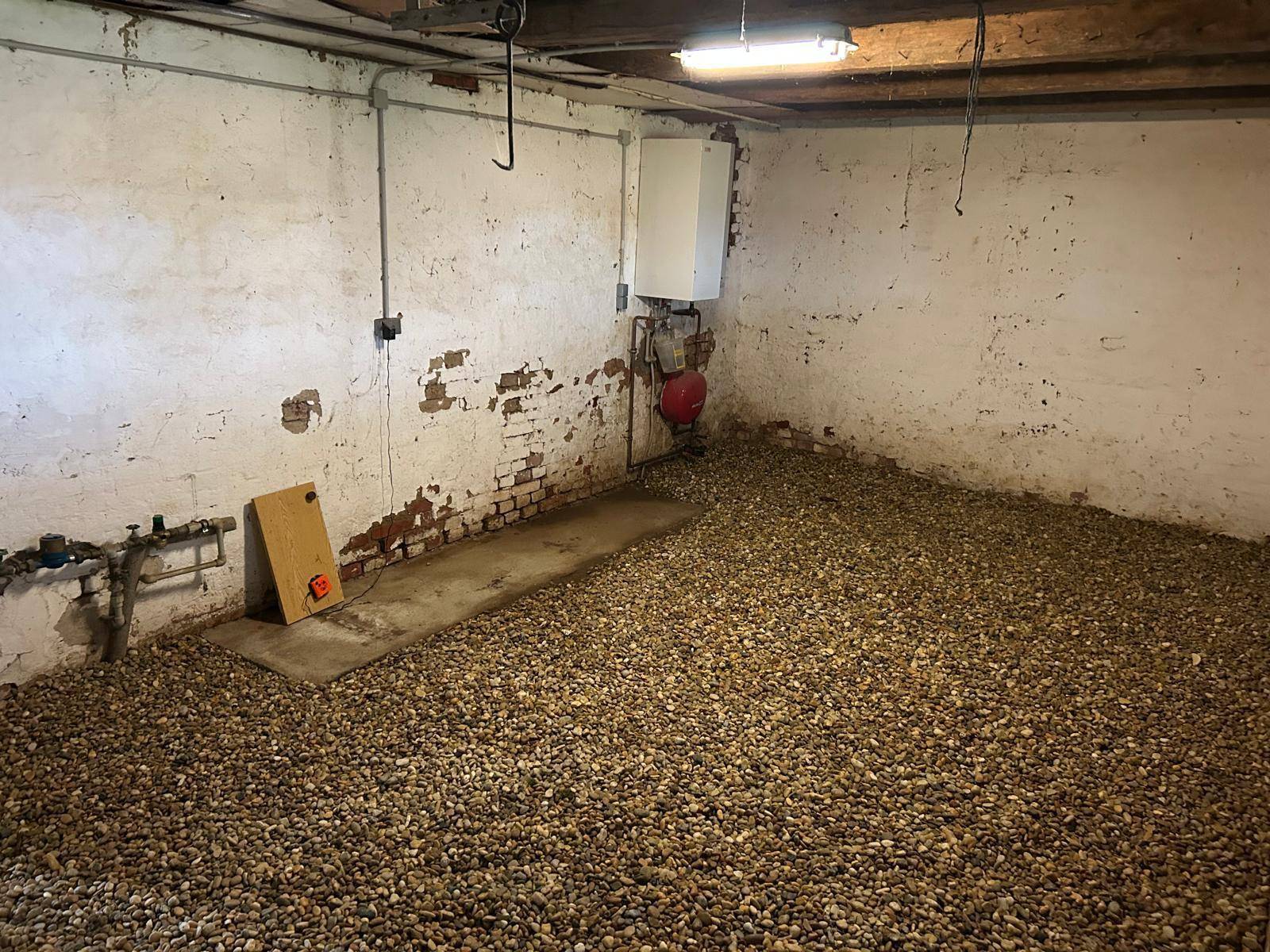 Unfertiger Kellerraum mit Kiesboden und sichtbaren Installationen.