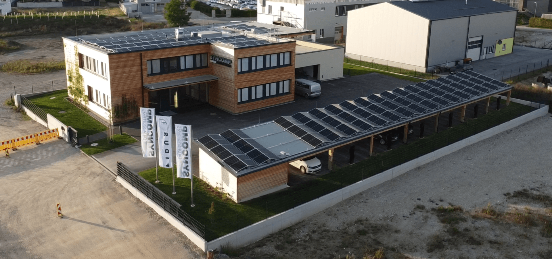 Luftaufnahme des Gebäudes mit Photovoltaikanlage auf dem Dach und überdachten Parkplätzen mit Solarmodulen.
