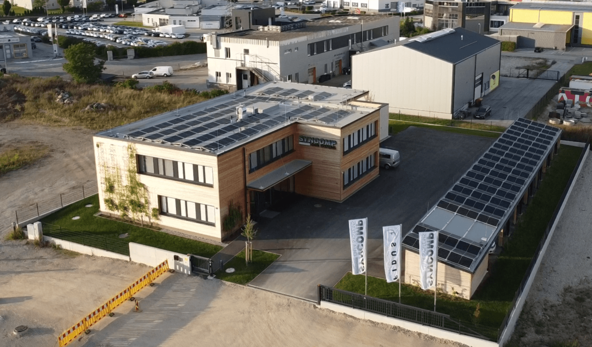 Weitläufige Luftaufnahme des modernen Geschäftsgebäudes mit Solaranlagen und umliegendem Industriegebiet.