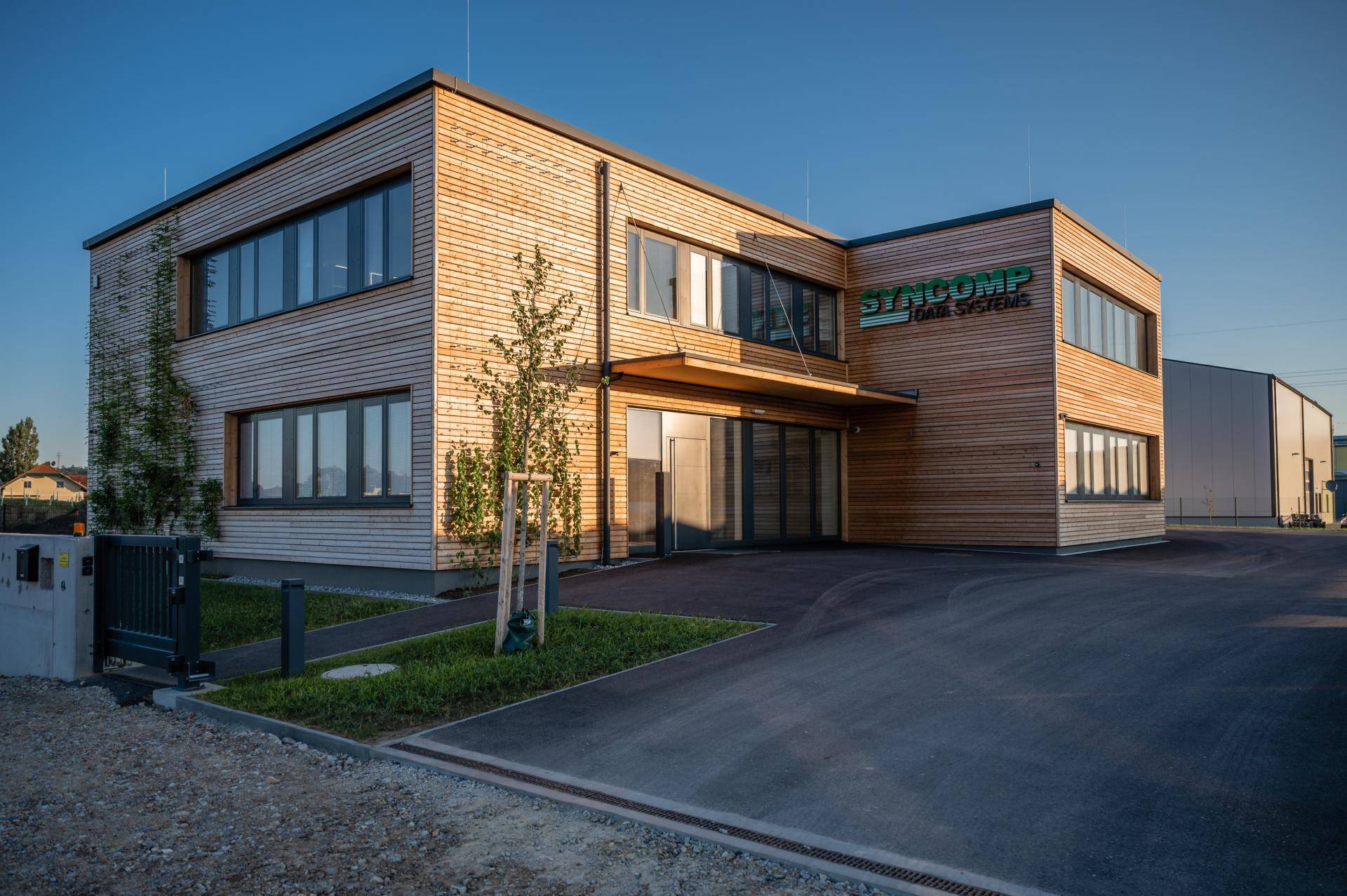 Modernes Geschäftsgebäude mit Holzfassade, großen Fenstern und gepflegter Grünfläche im Vordergrund.
