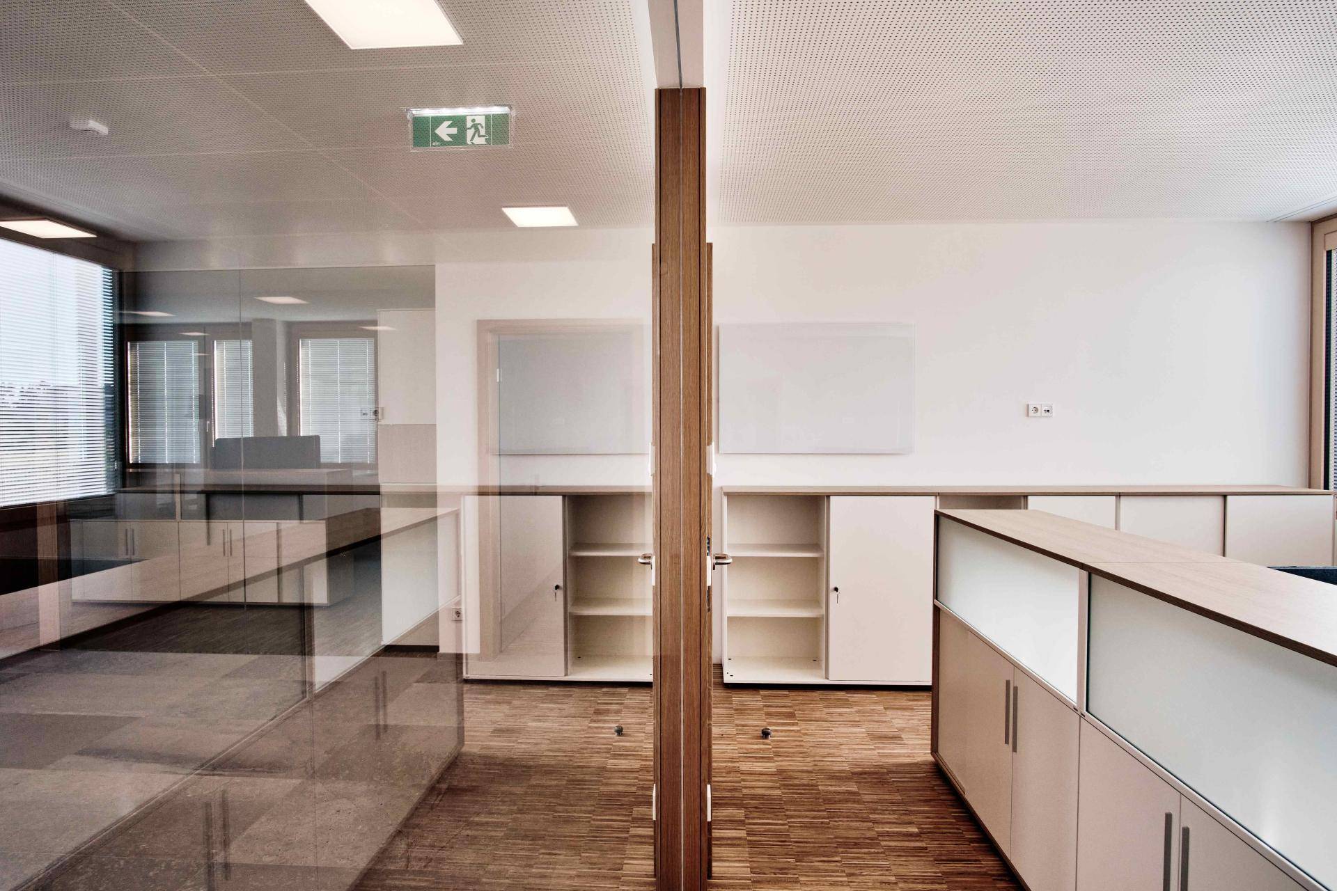 Offener Bürobereich mit Glaswänden, Holzböden und modernen Schränken.