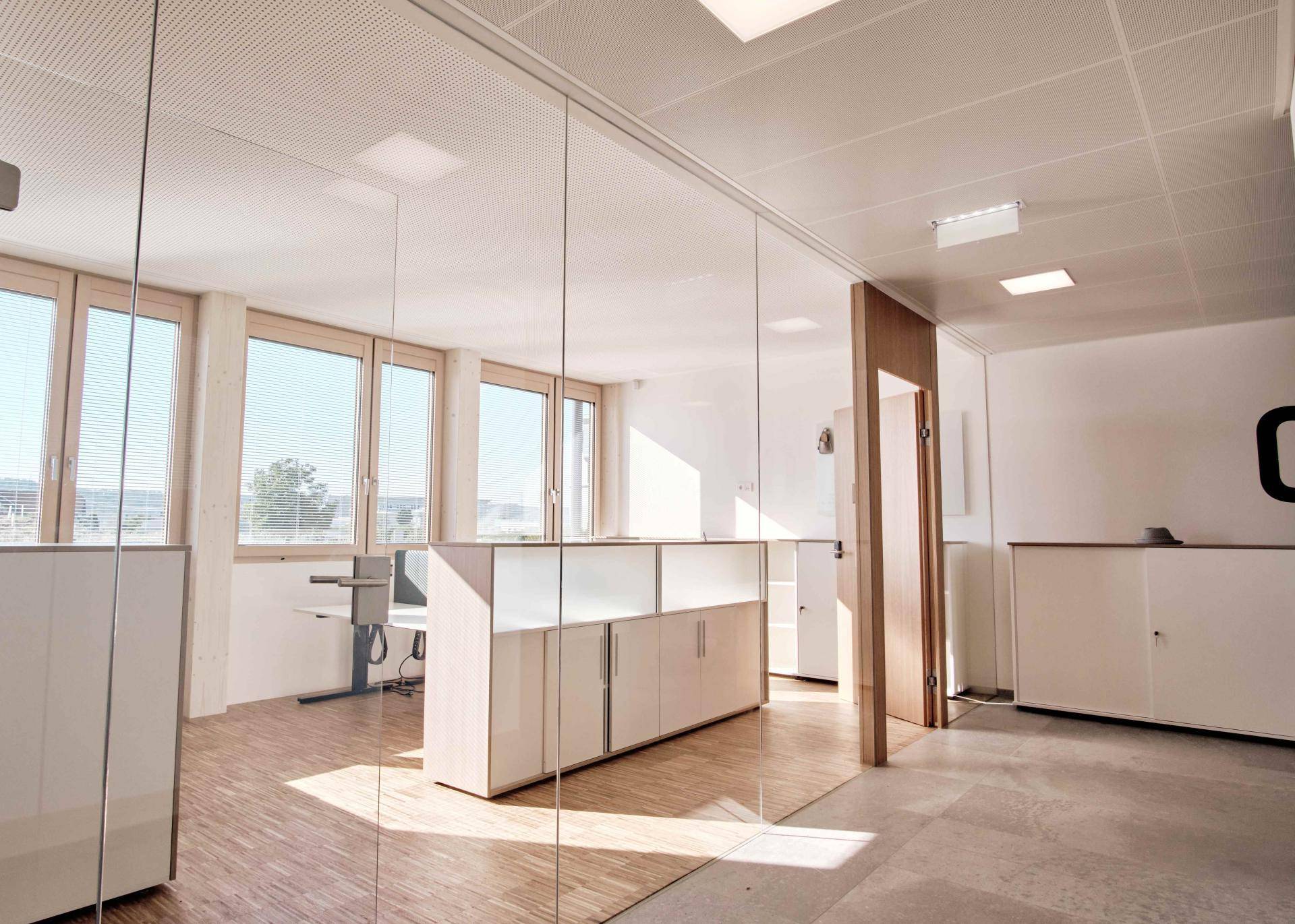 Geräumiger Bürobereich mit Glaswänden, Holzboden und viel natürlichem Licht.