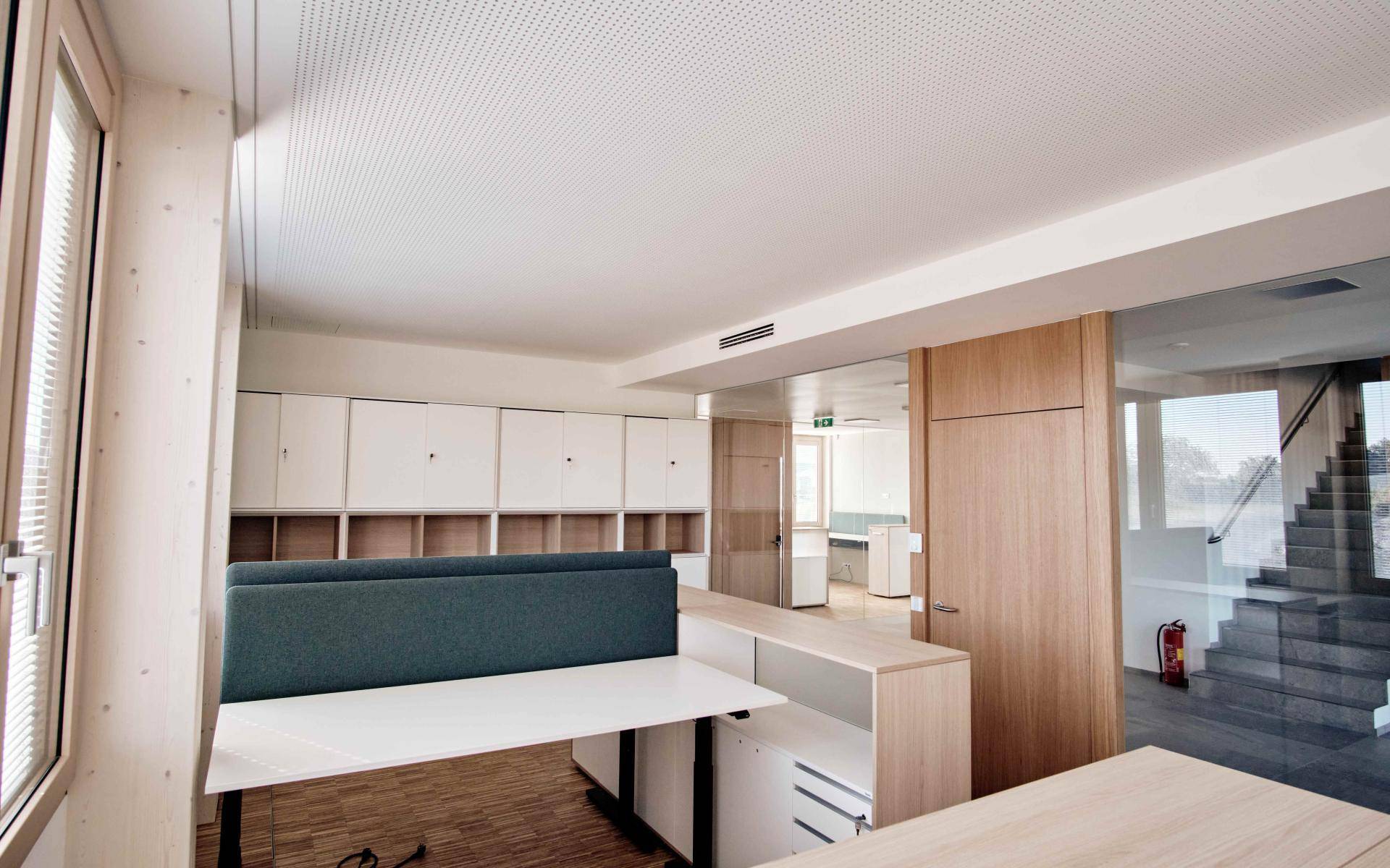 Moderner Bürobereich mit Schreibtischen, Stauraum und Blick auf das Treppenhaus.