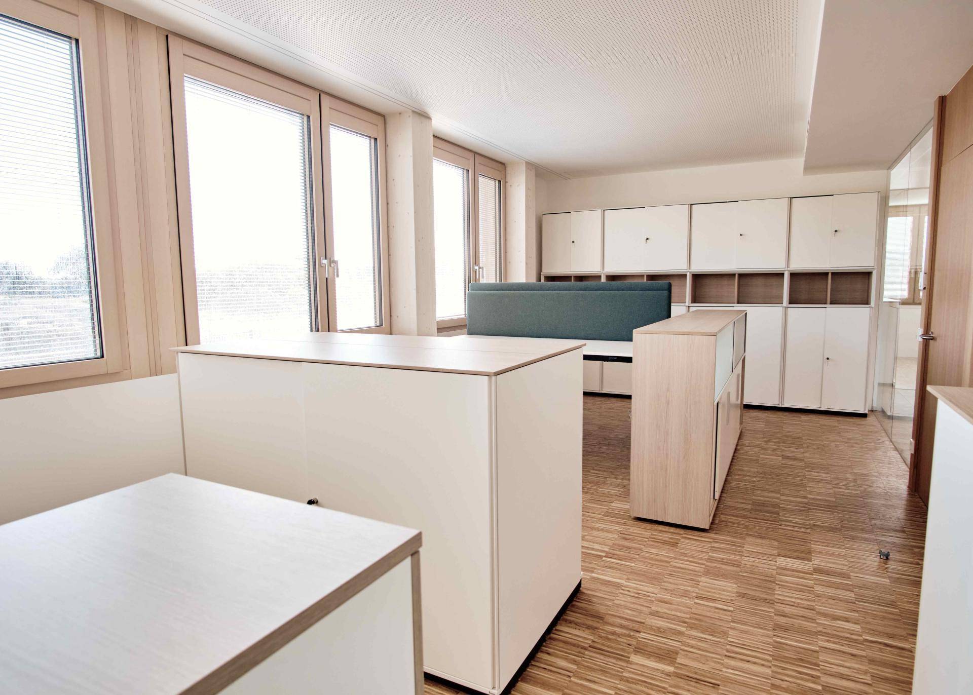Offener Büroraum mit integrierten Schränken, Holzboden und großen Fenstern.