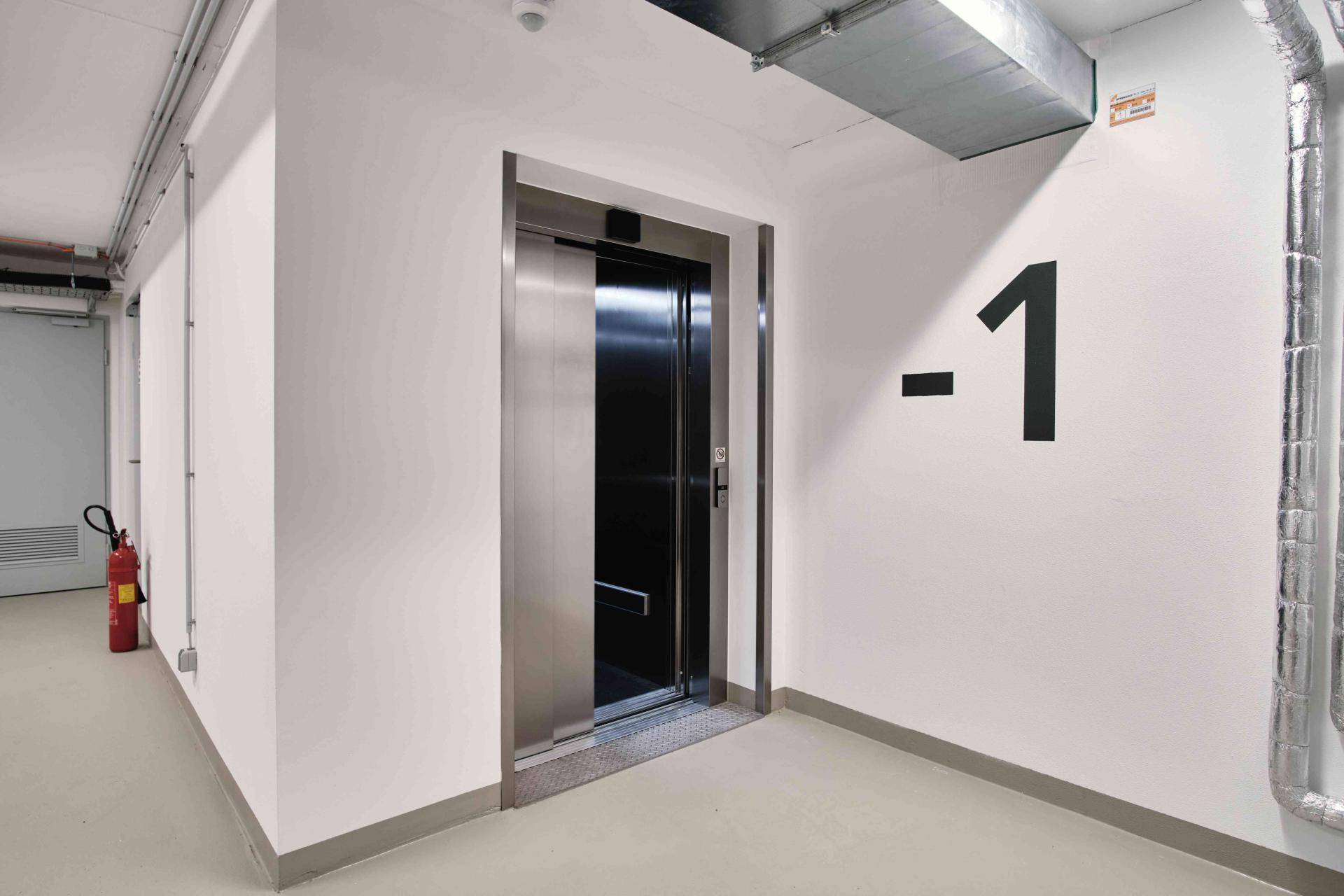 Kellerbereich mit modernem Aufzug und sichtbaren Installationen an der Decke.