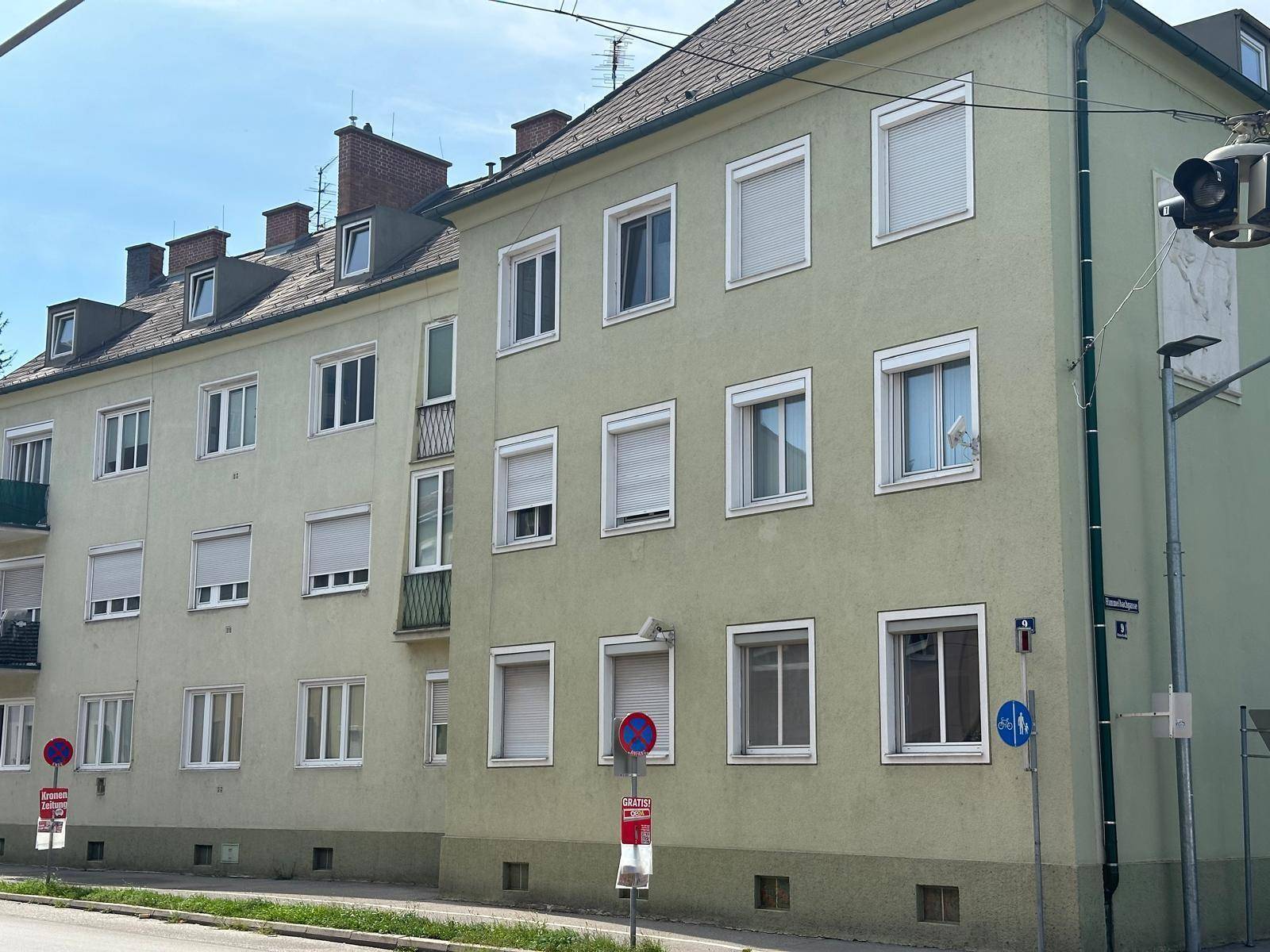 Mehrfamilienhaus mit hellgrüner Fassade, vielen Fenstern und Rollläden.