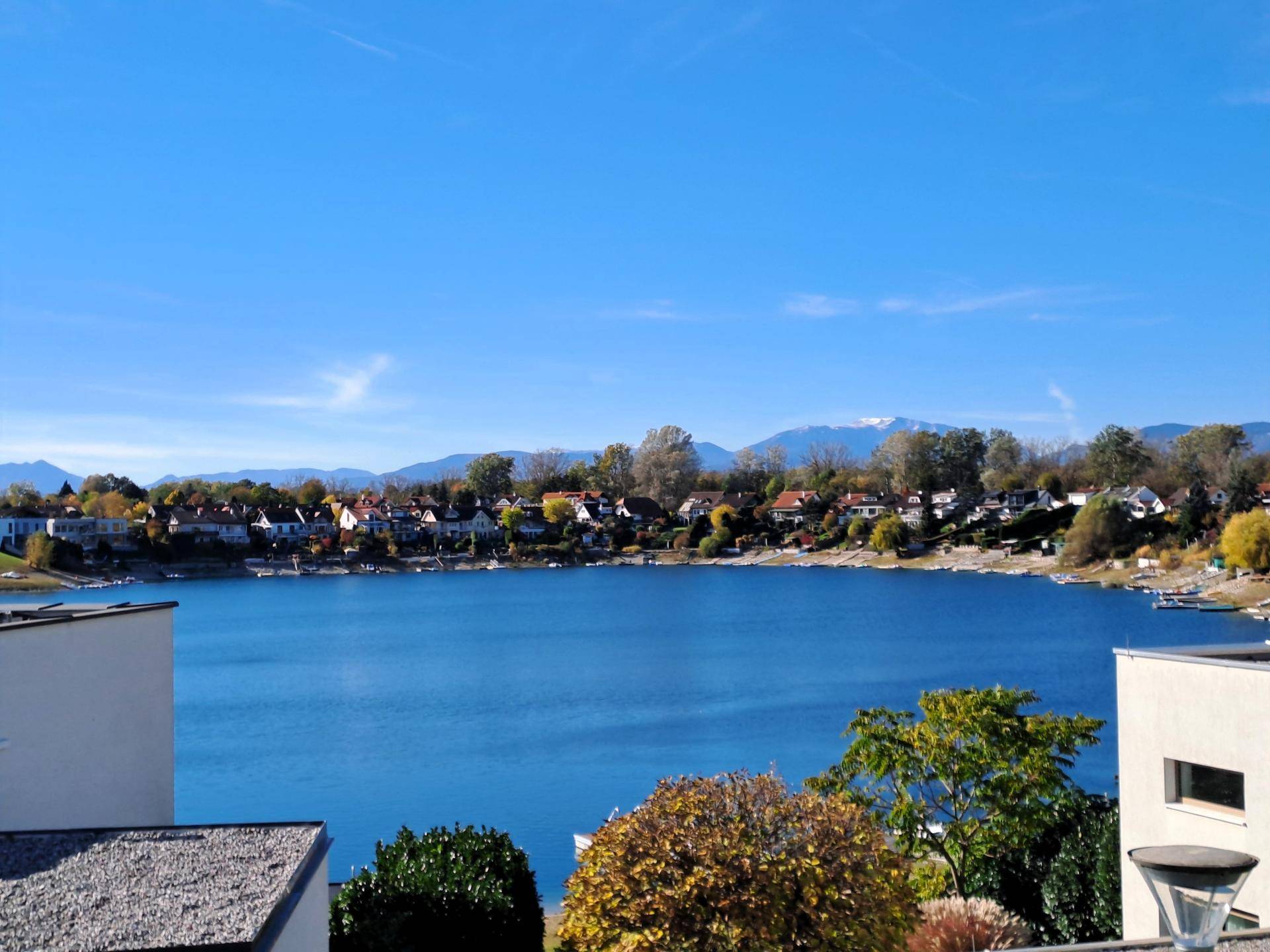 Panoramablick auf den See mit umliegenden Häusern und einer beeindruckenden Bergkulisse im Hintergrund.