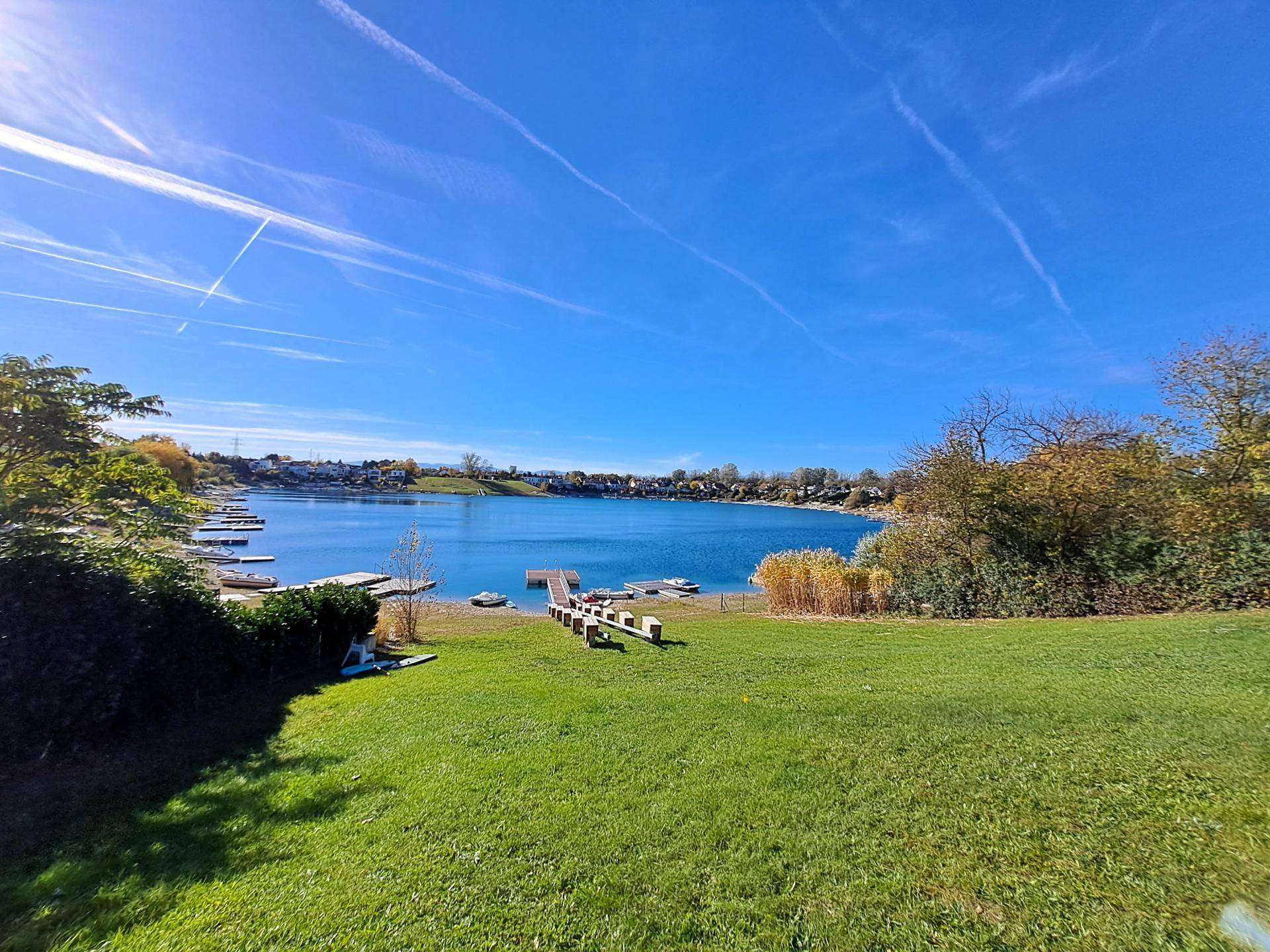 Weitläufige Rasenfläche am Seeufer mit Blick auf das klare Wasser und die grüne Umgebung.
