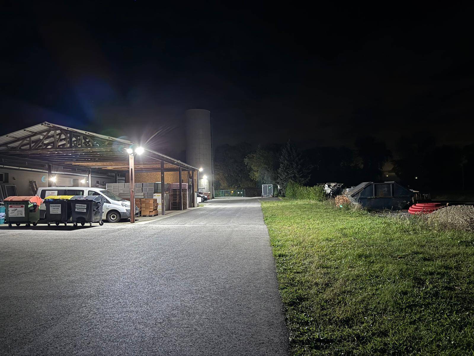 Nachtansicht des überdachten Lagerbereichs und des angrenzenden Grüns, beleuchtet von Außenlampen.