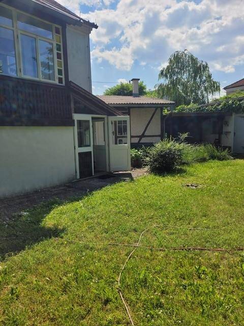 Hinterhof mit Rasenfläche und Zugang zum Haus, umgeben von viel Grün und Bäumen.