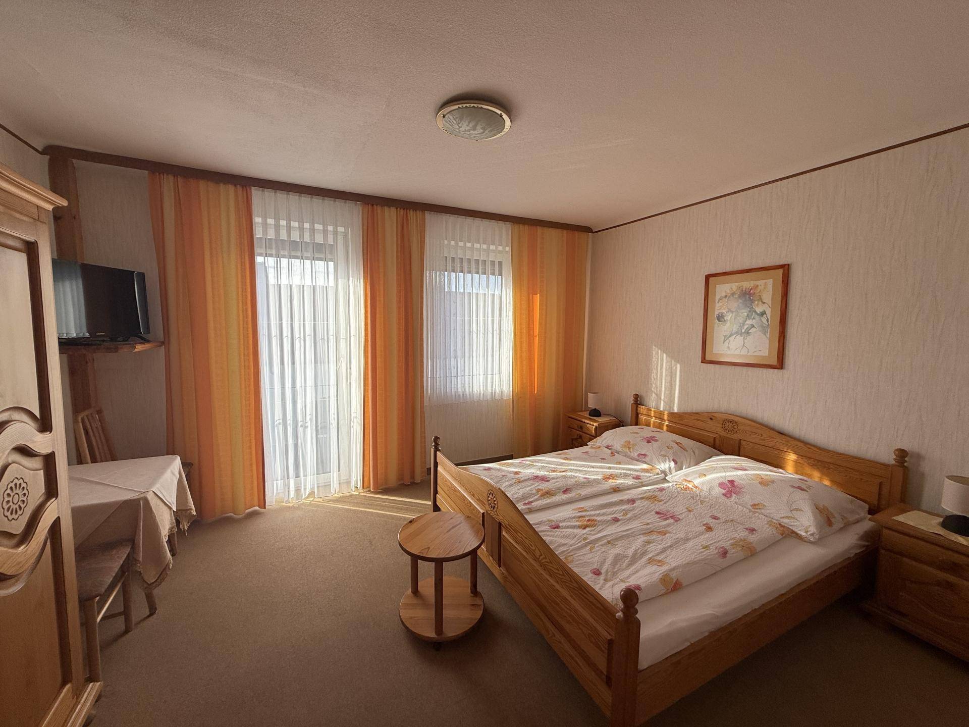 Gemütliches Schlafzimmer mit Doppelbett, Holzmöbeln und Teppichboden, durchflutet von Sonnenlicht.
