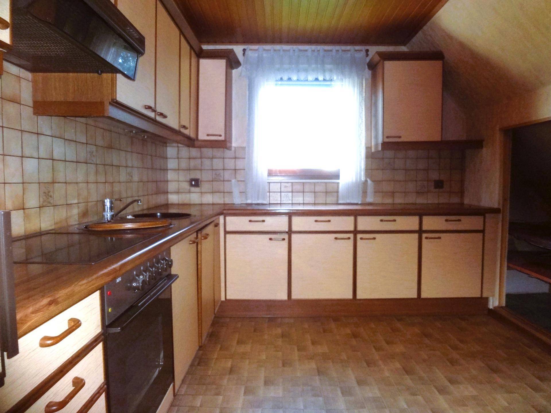Ältere Küche mit Holzschränken, Fliesenrückwand und Fenster.