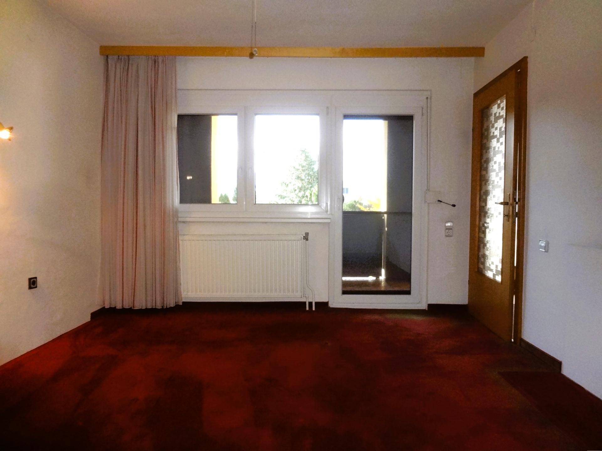 Wohnzimmer mit rotem Teppichboden und Zugang zu einem Balkon.