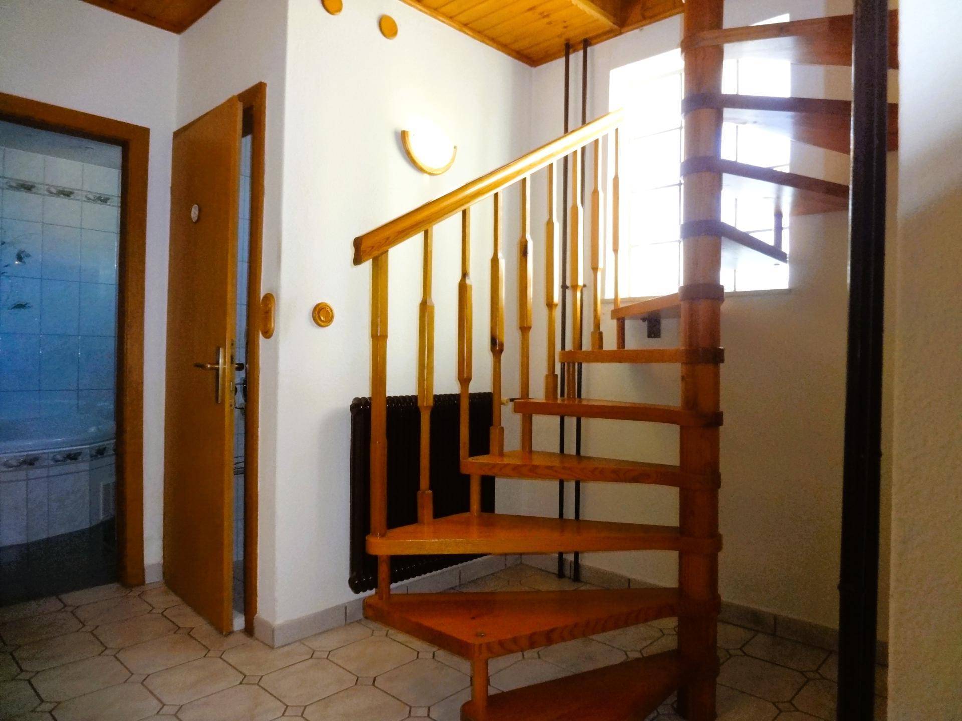 Flur mit Wendeltreppe aus Holz, Fliesenboden und Zugang zum Badezimmer.