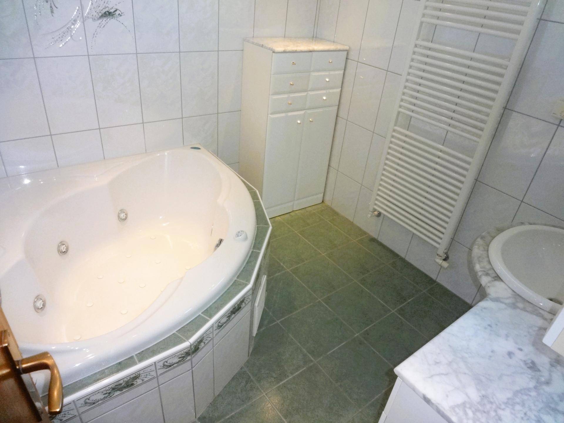 Badezimmer mit Eckbadewanne, Whirlpool-Funktion, Fliesen und beheiztem Handtuchhalter.