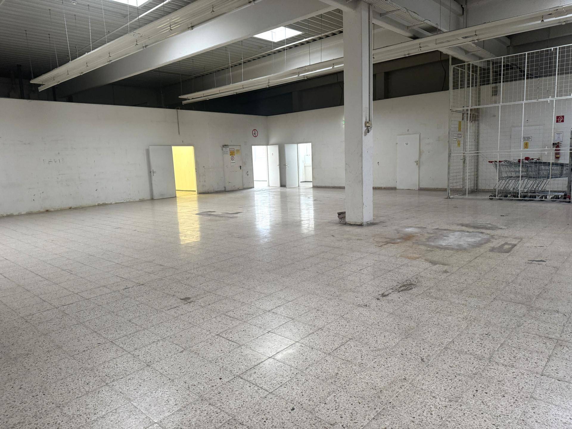 Ecke eines großen Ladenlokals mit Fliesenboden, tragender Säule und mehreren Türen.
