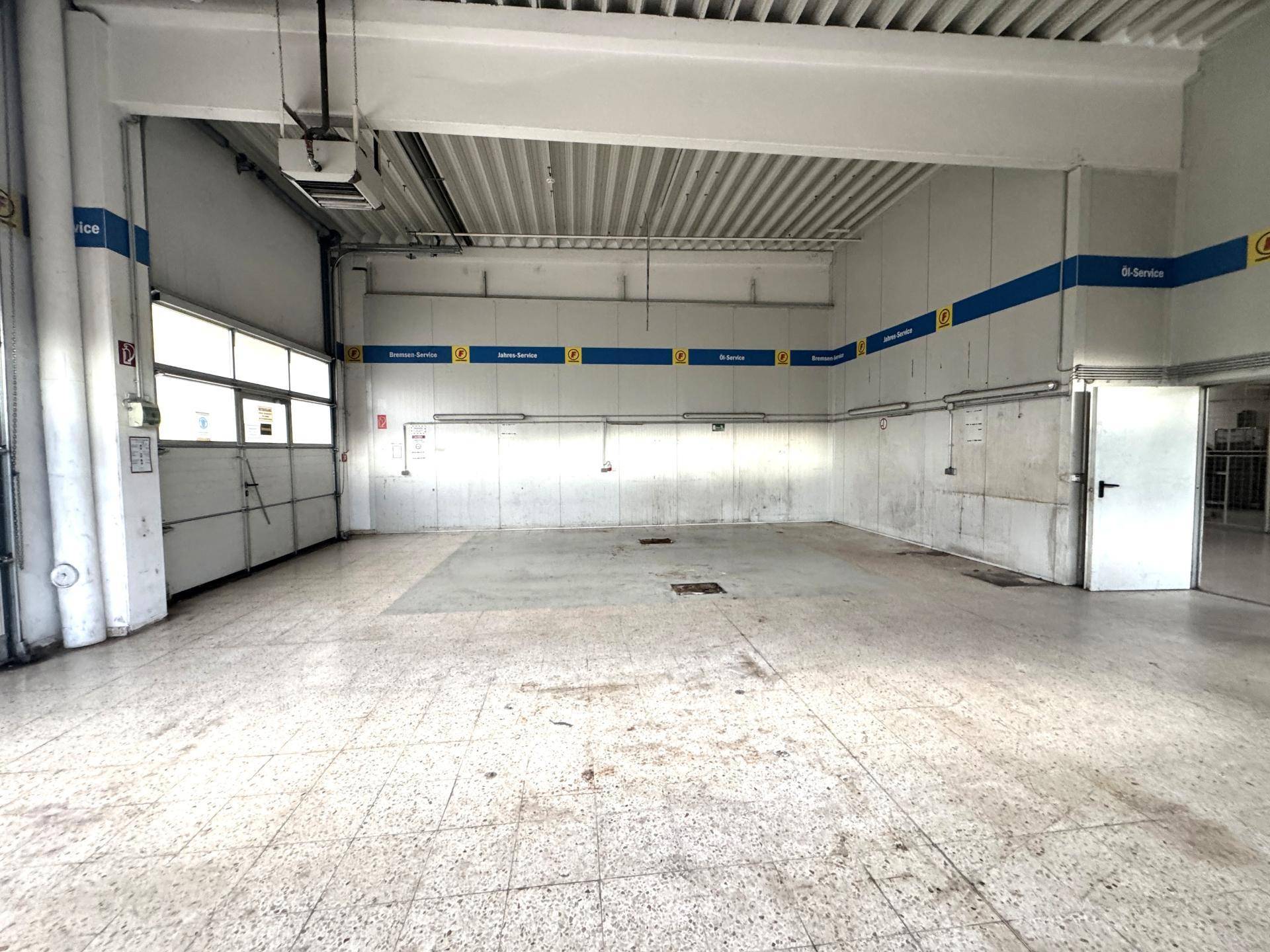 Große Garage oder Werkstatt mit Rolltor, Fliesenboden und Service-Markierungen an den Wänden.