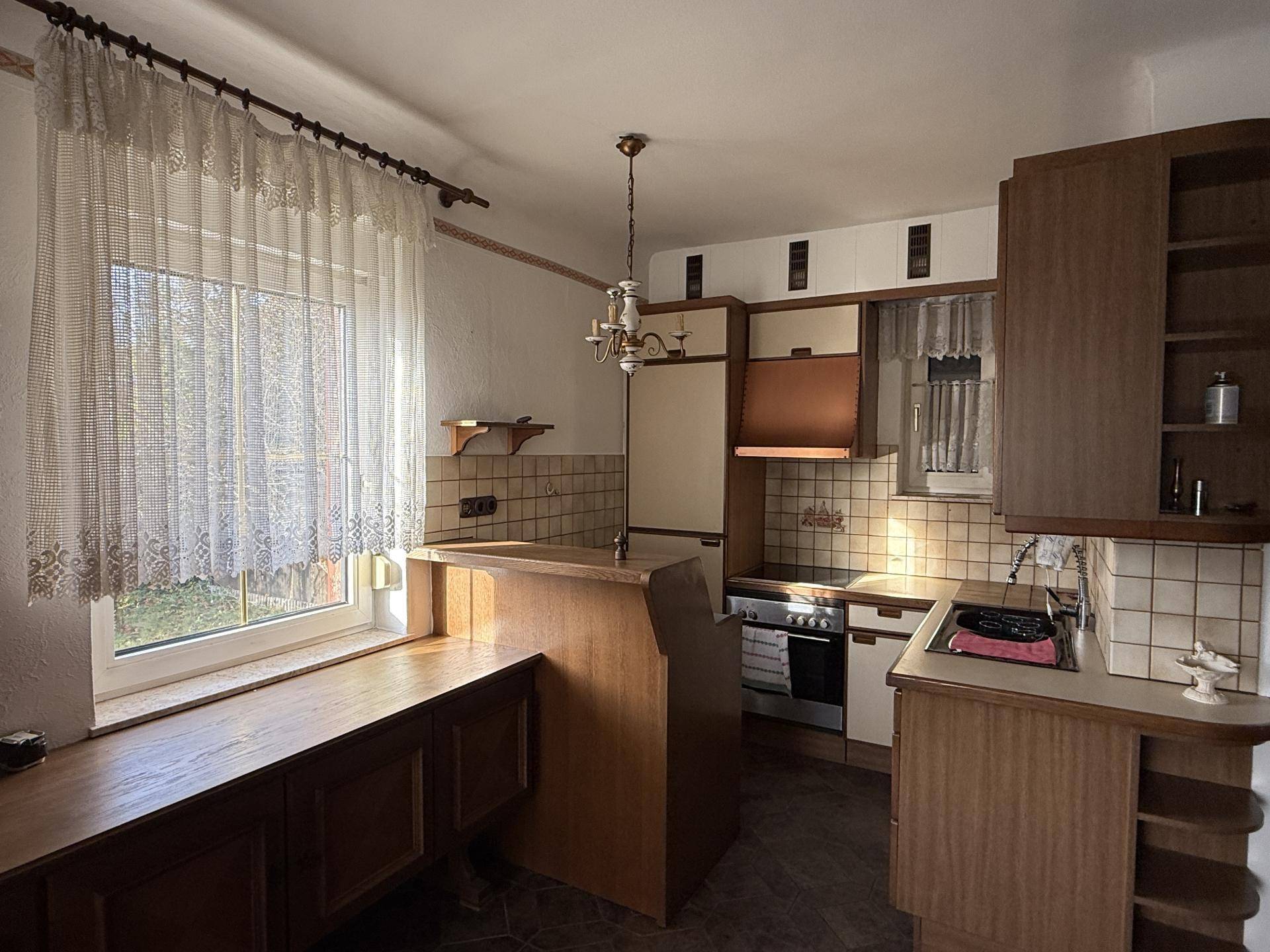Rustikale Küche mit Holzmöbeln, Fliesenboden und Fenster mit Blick ins Grüne.