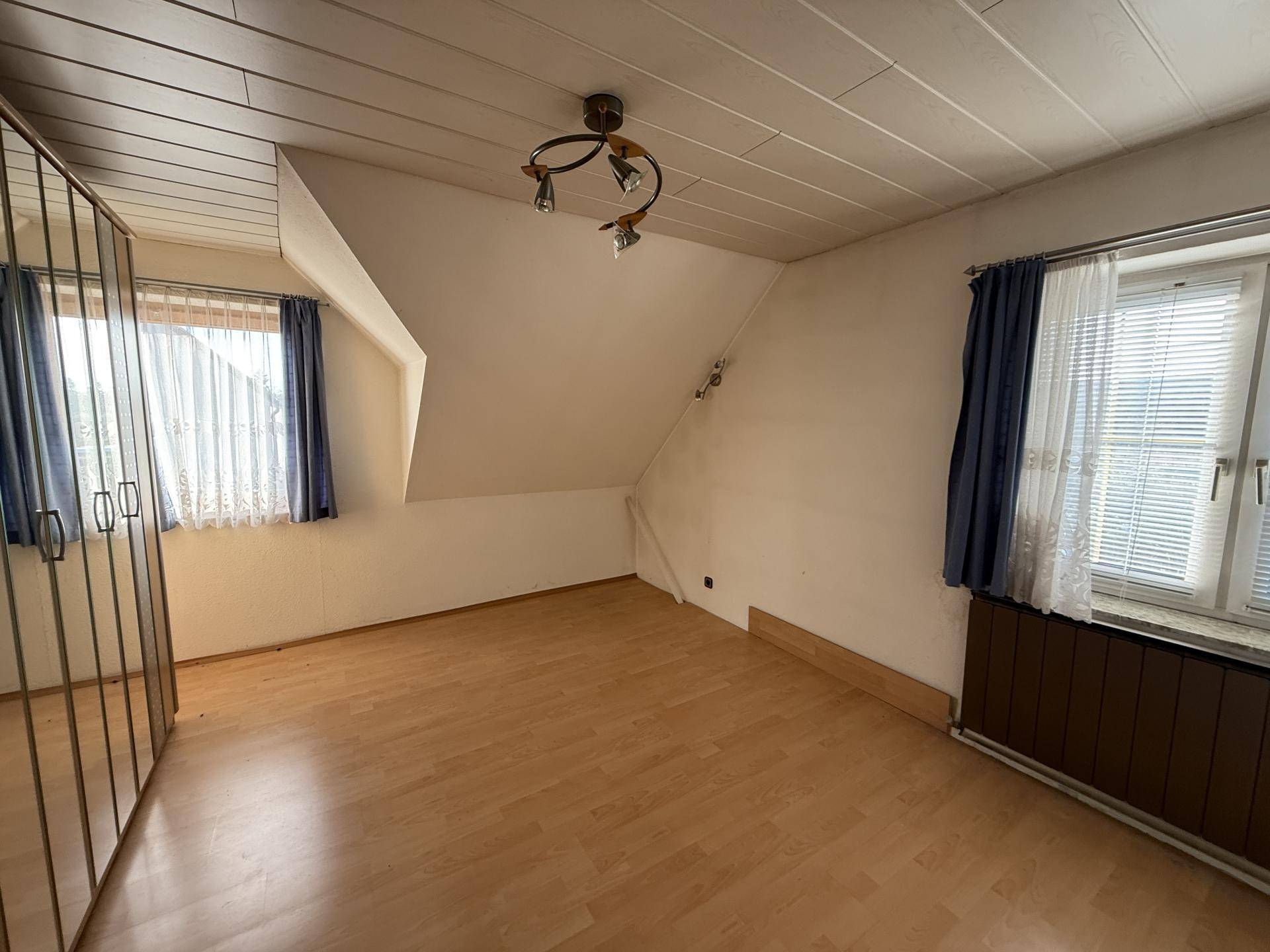 Schlafzimmer im Dachgeschoss mit Laminatboden, Dachschräge und Spiegelschrank.