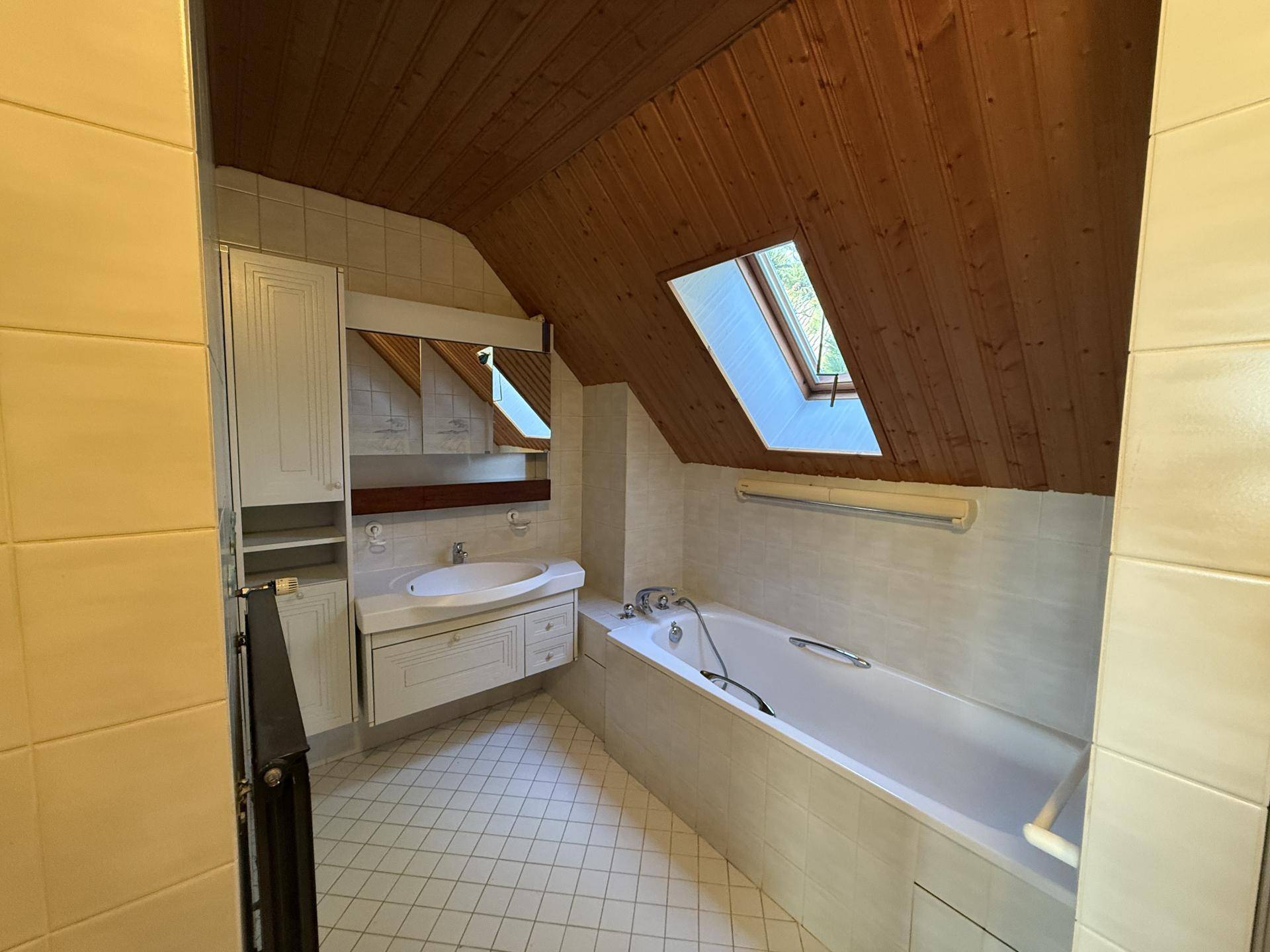Badezimmer im Dachgeschoss mit Badewanne, Dachfenster und Holzdecke.