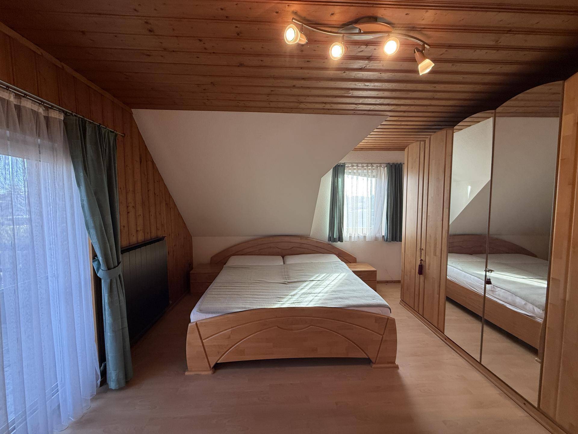 Helles Schlafzimmer im Dachgeschoss mit Holzbett, Spiegelschrank und Holzdecke.