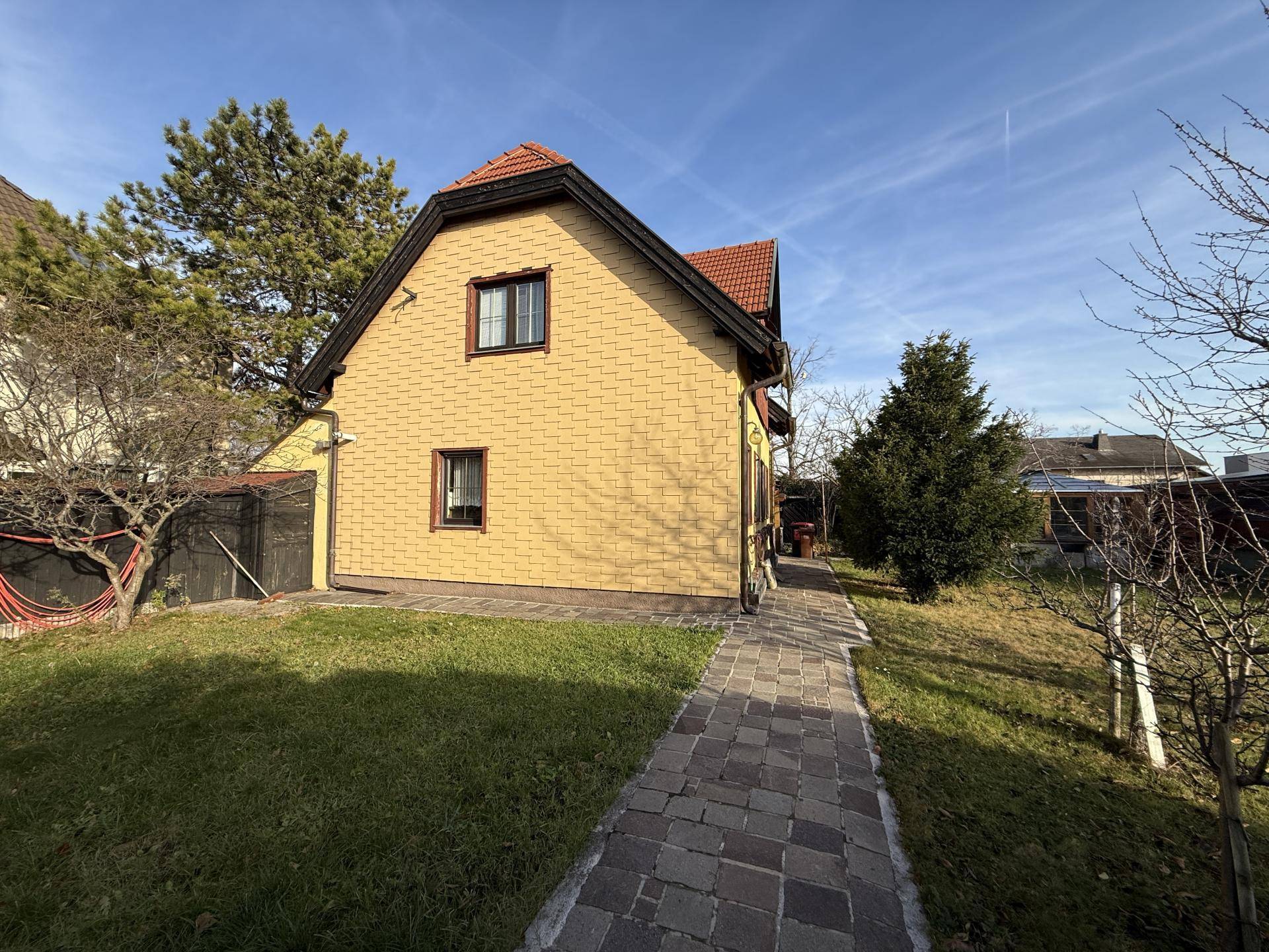 Seitenansicht des Hauses mit gepflastertem Weg und grünem Rasen.