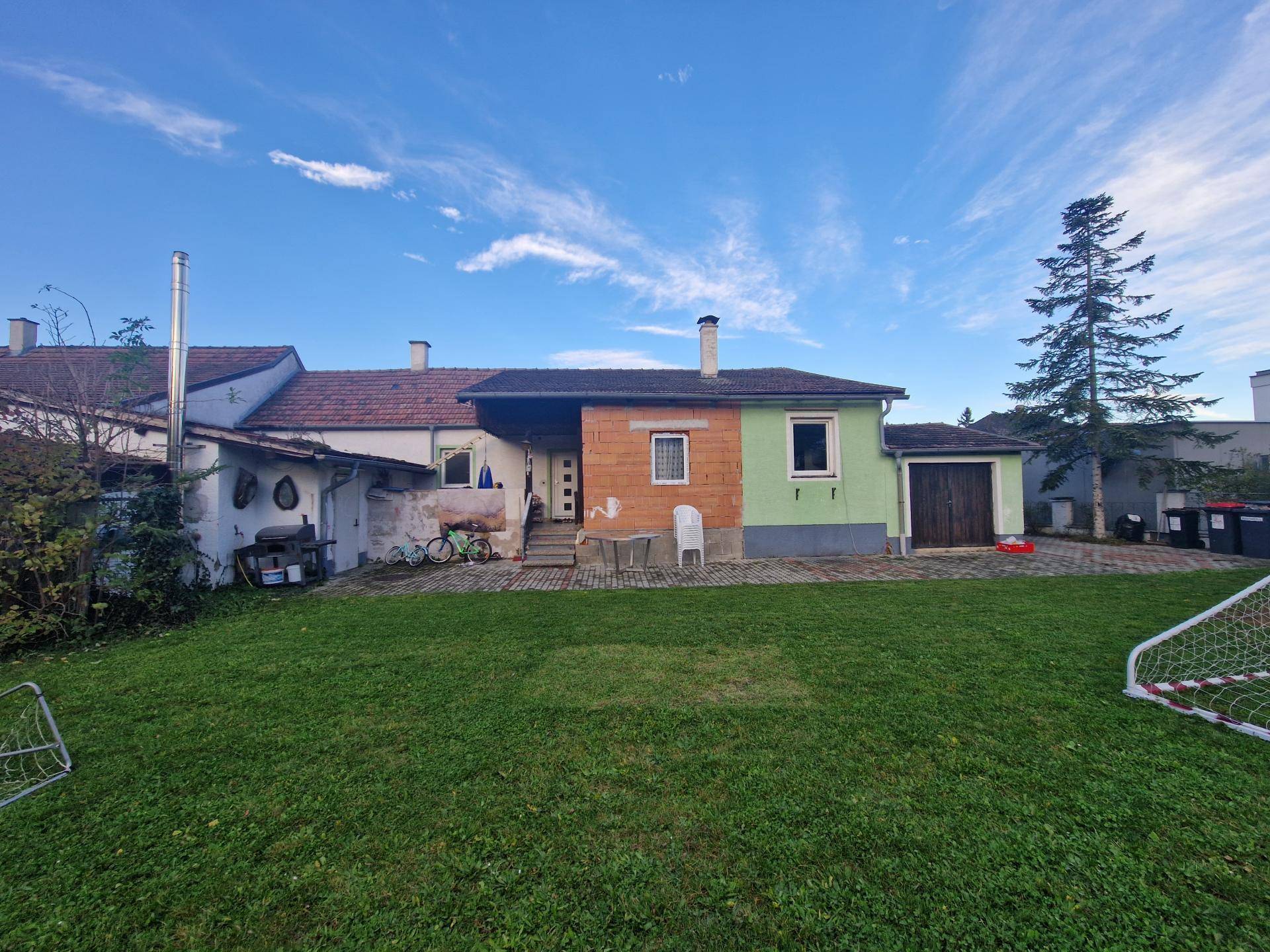 Rückansicht des Hauses mit großem Garten, kleiner Terrasse und angrenzender Garage.