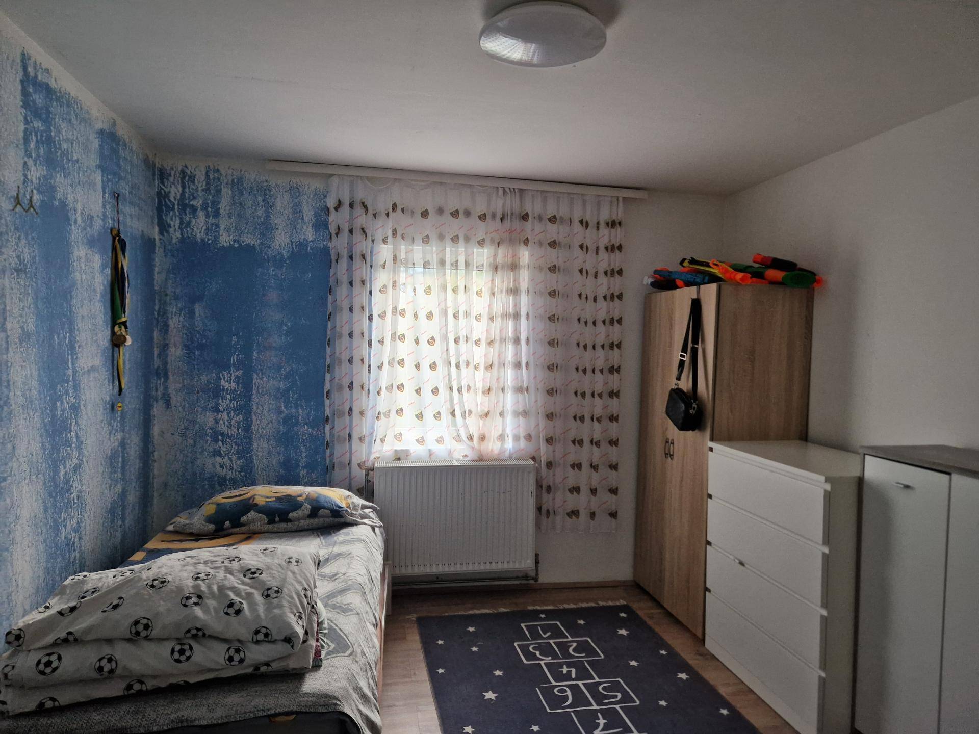 Kinderzimmer mit Einzelbett, Schrank und einer kreativ gestalteten blauen Wand.