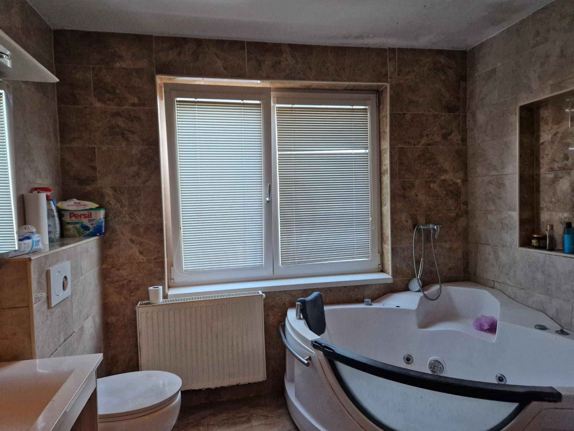 Badezimmer mit braunen Fliesen, Eckbadewanne mit Whirlpoolfunktion und Fenster.