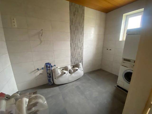 Badezimmer in Renovierung mit neuen Fliesen, Holzdecke und vorbereiteten Anschlüssen für Sanitäranlagen.