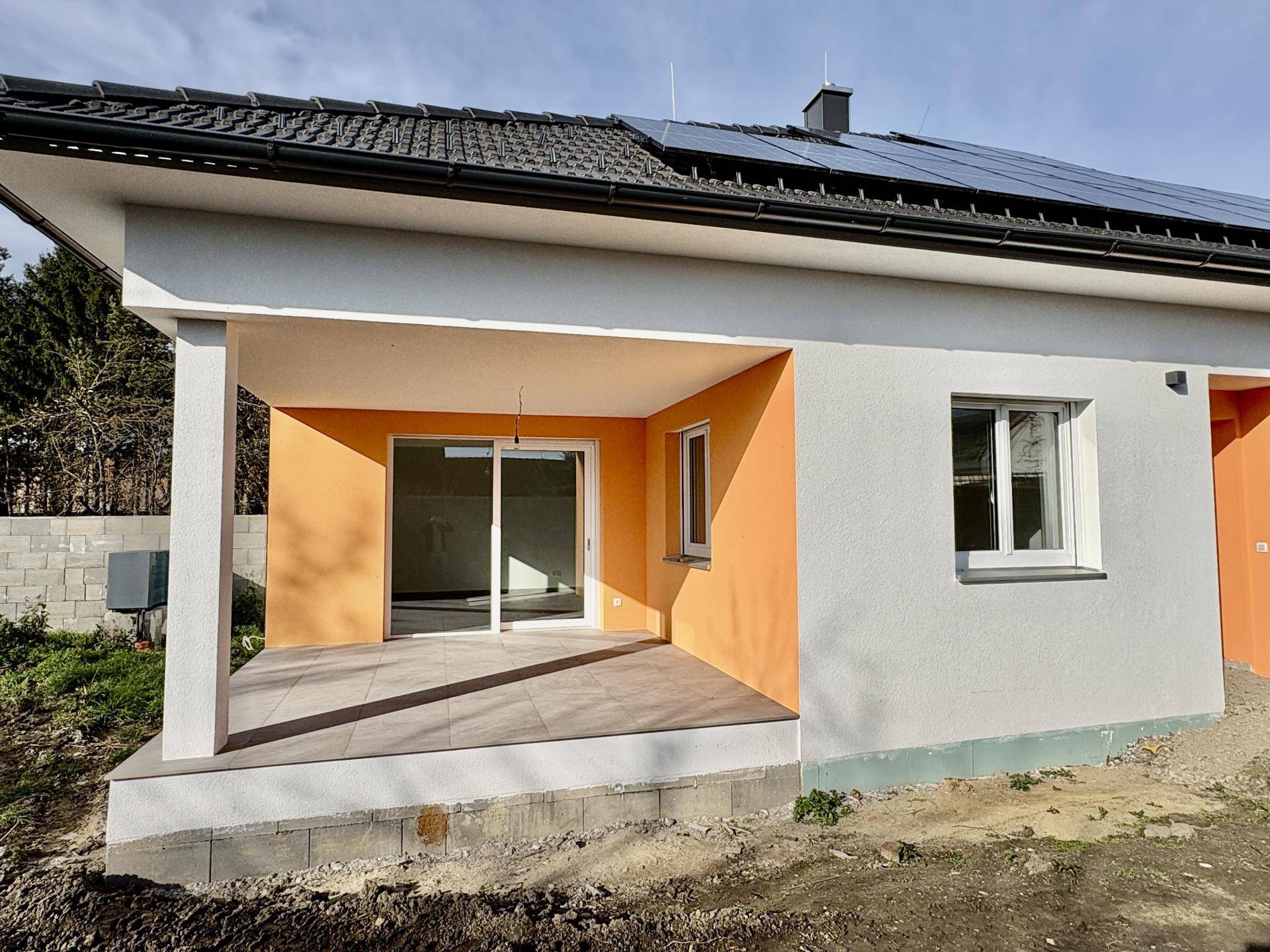 Überdachte Terrasse mit Fliesenboden und Zugang zum Innenbereich des Neubaus.