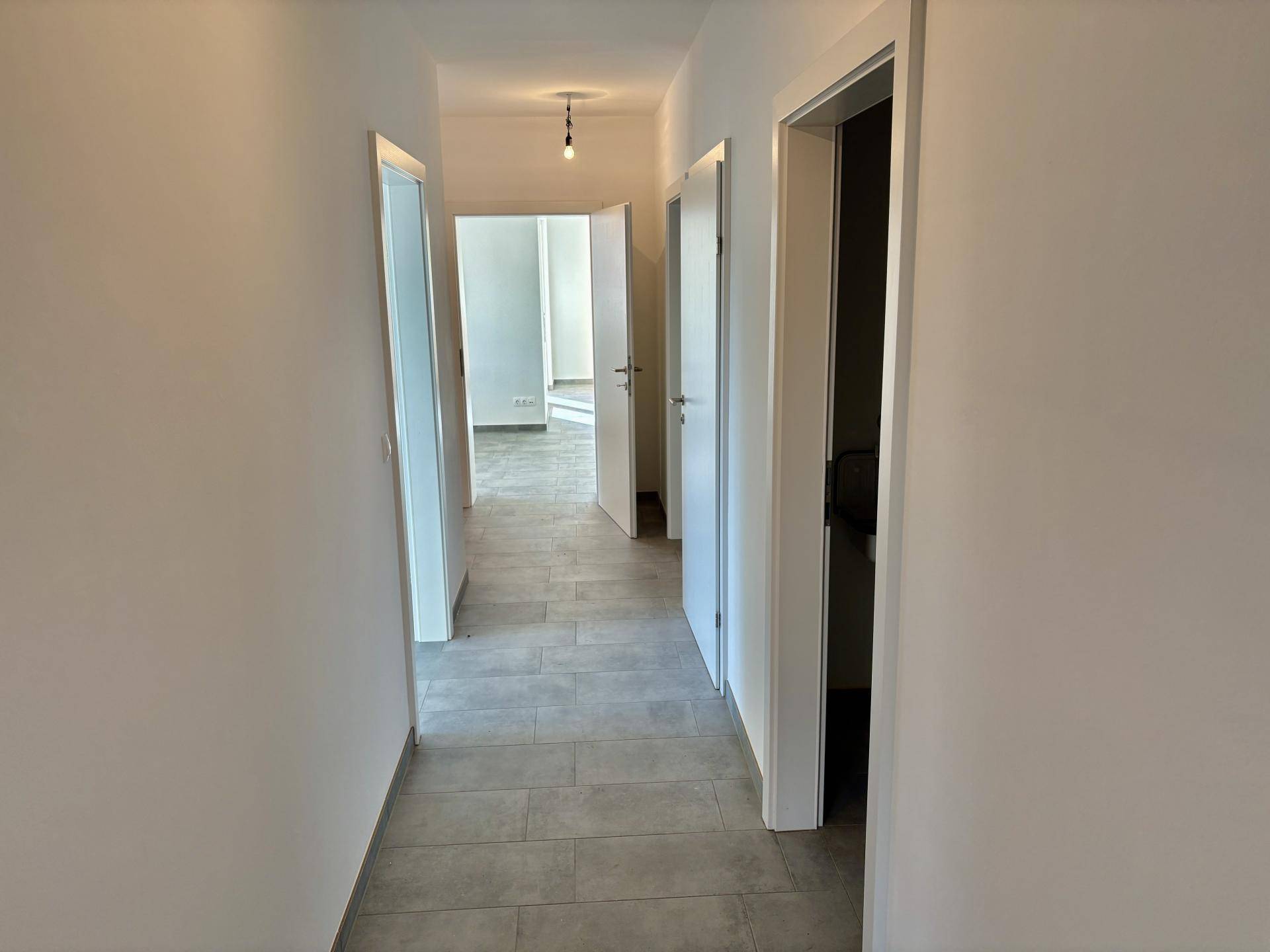 Langer, heller Flur mit grauen Fliesen und weißen Türen, der zu weiteren Räumen führt.