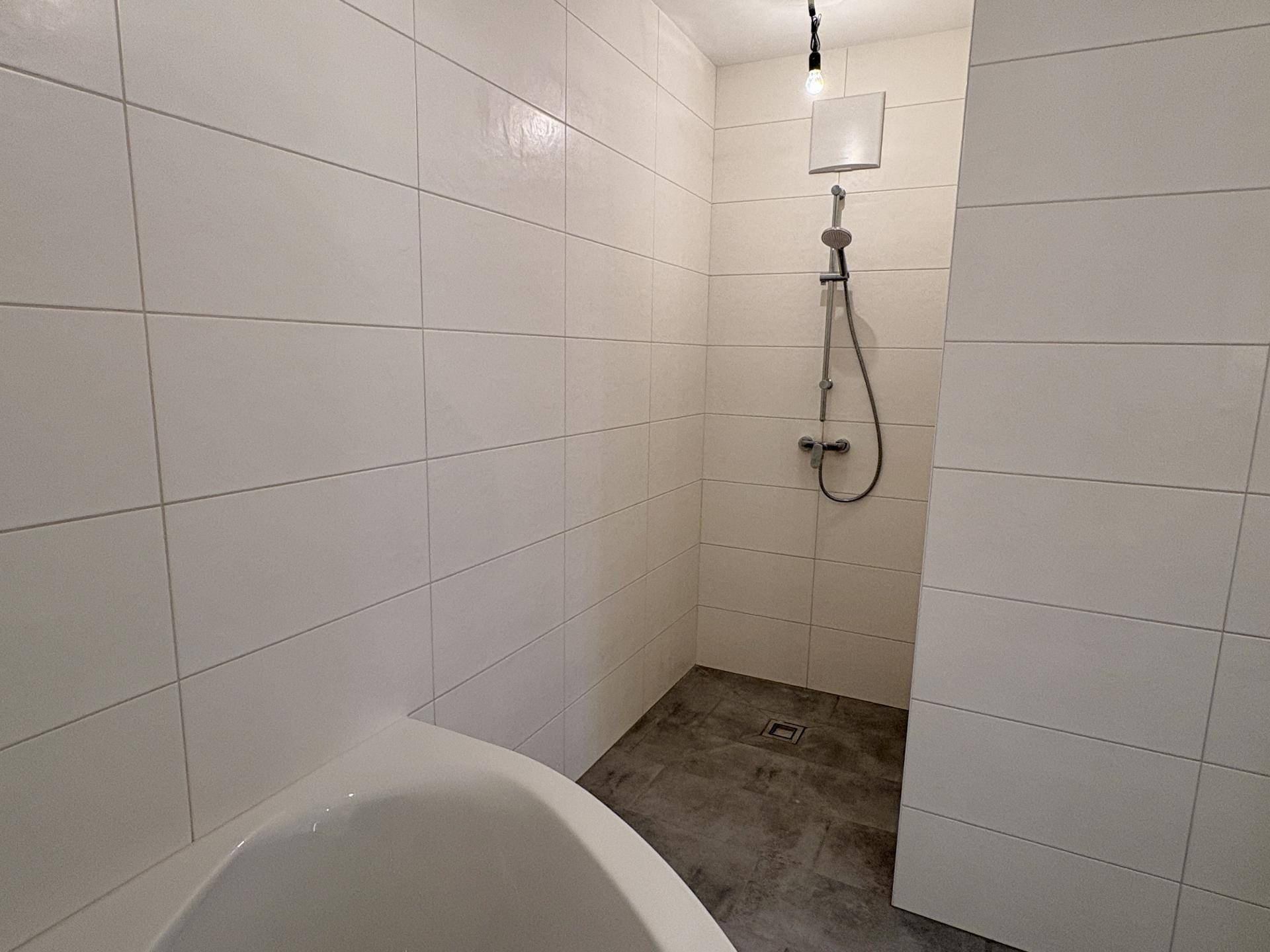 Duschbereich im Badezimmer mit weißen Wandfliesen und ebenerdigem Zugang.