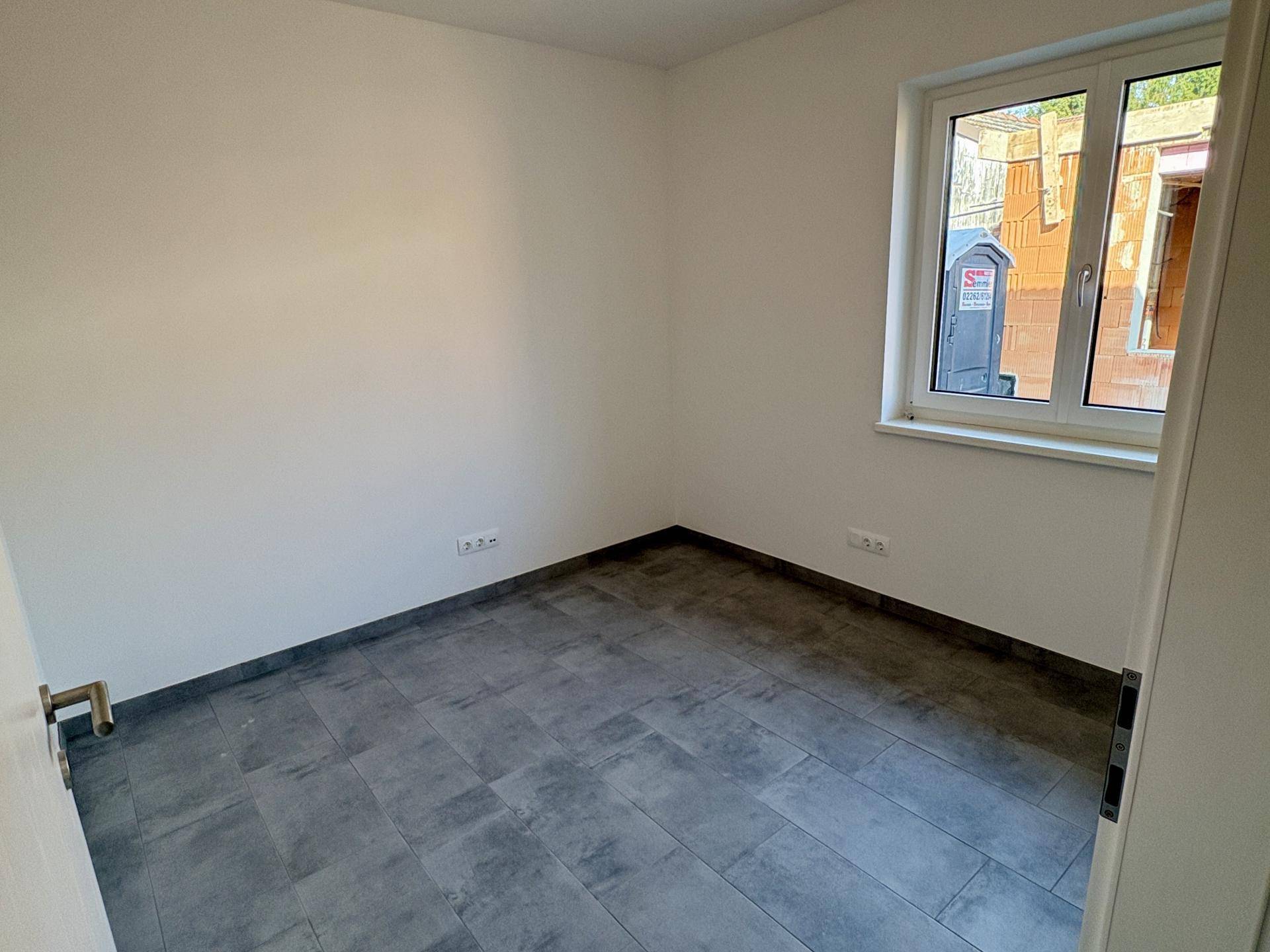 Kleineres Schlafzimmer mit Fliesenboden und Fenster, das viel Tageslicht hereinlässt.