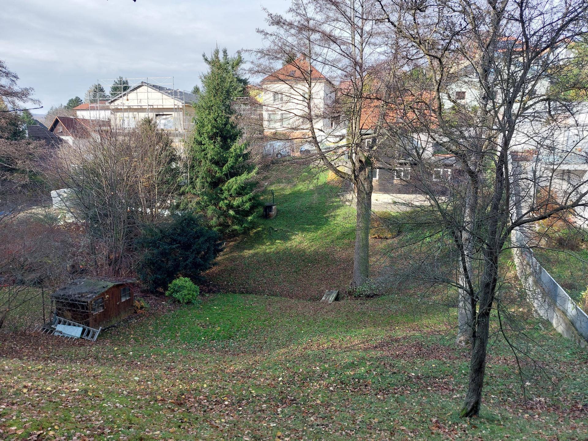 Weitläufiger Gartenbereich mit Bäumen, Rasen und einem kleinen Gartenhaus in der Ferne.