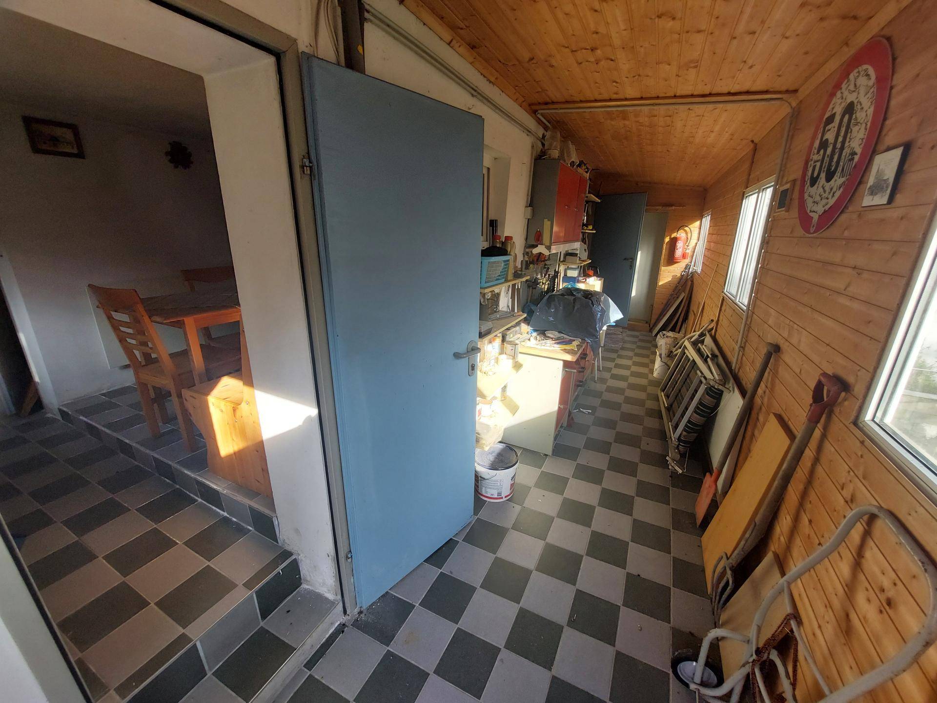 Funktionaler Raum mit kariertem Fliesenboden, Holzverkleidung und Zugang zu einem weiteren Zimmer.