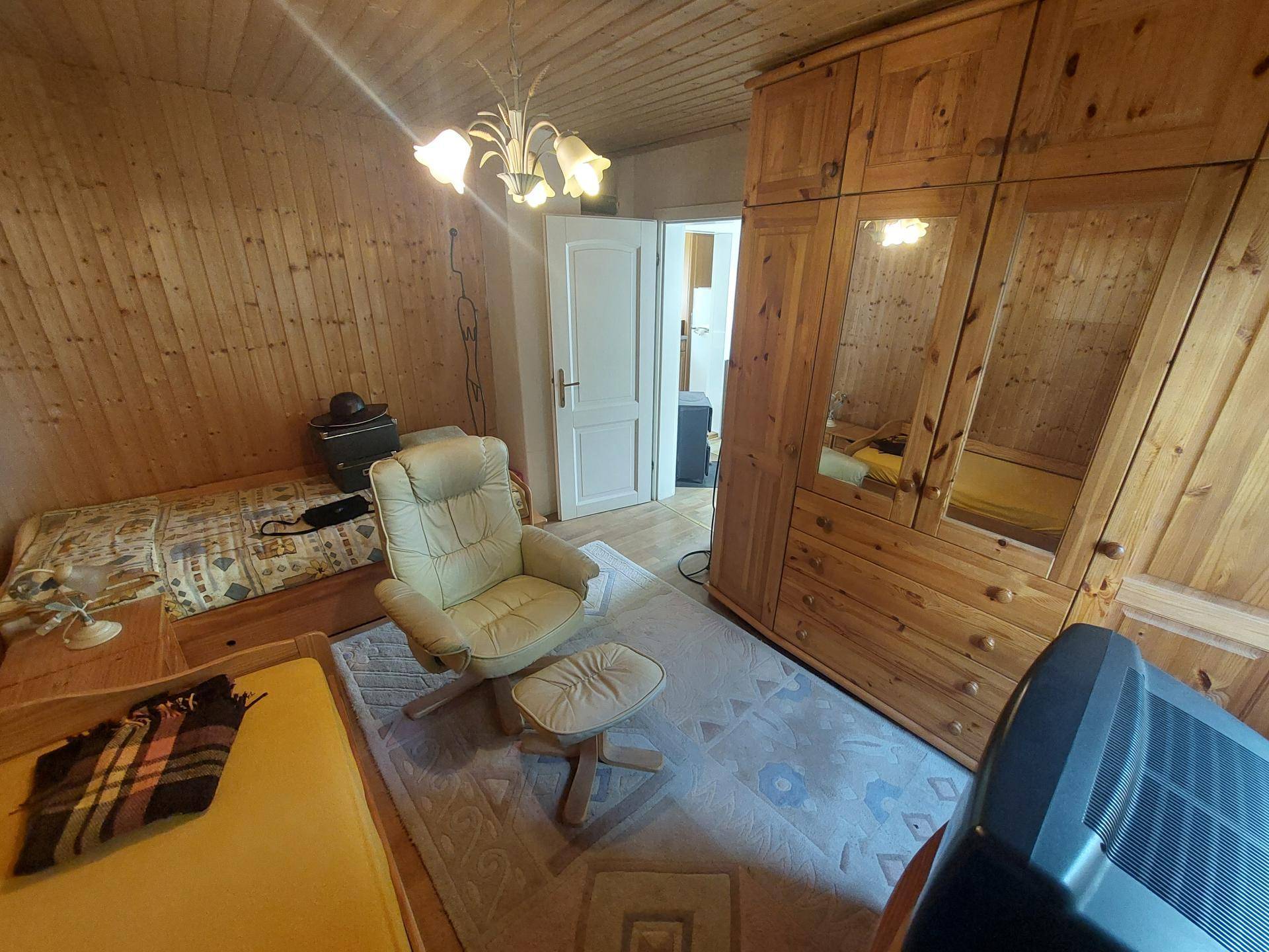 Schlafzimmer mit Holzvertäfelung, Einzelbett und einem großen Holzschrank mit Spiegeln.
