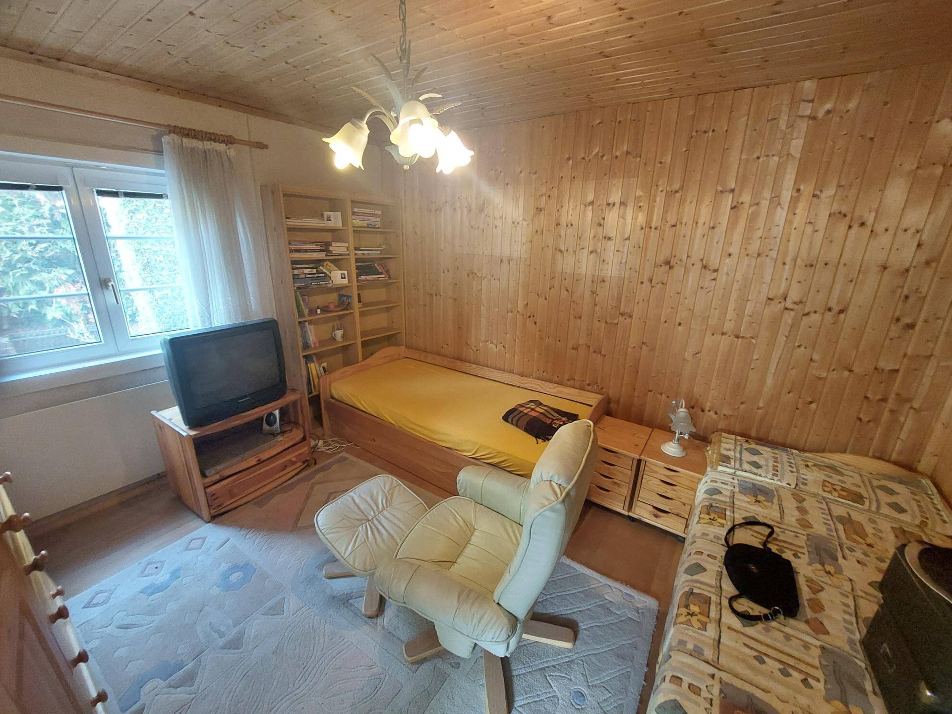 Helles Schlafzimmer mit Holzvertäfelung, zwei Einzelbetten und einem Sessel am Fenster.