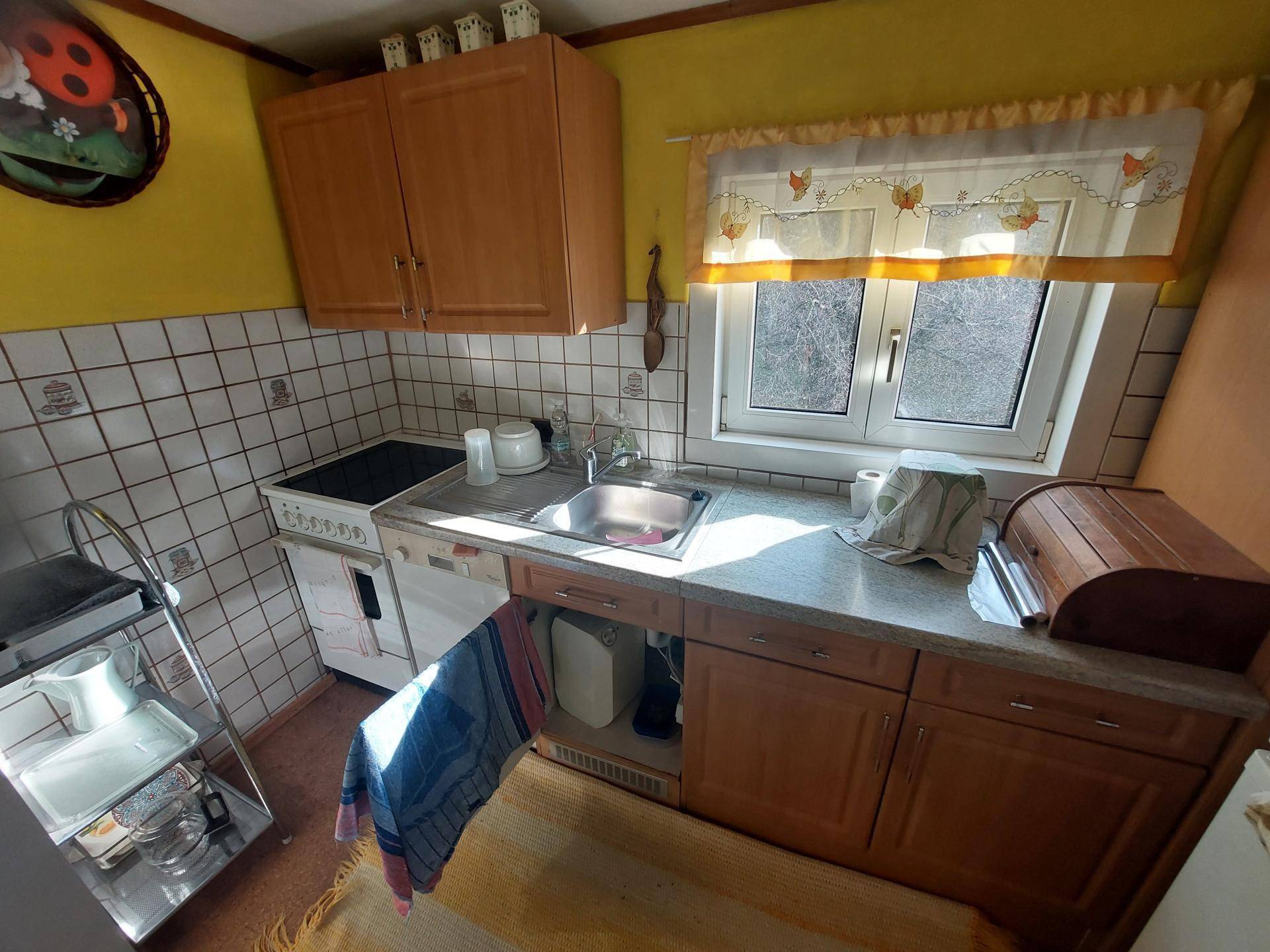 Kleine Küche mit Holzschränken, weiß gefliestem Spritzschutz und einem Fenster.