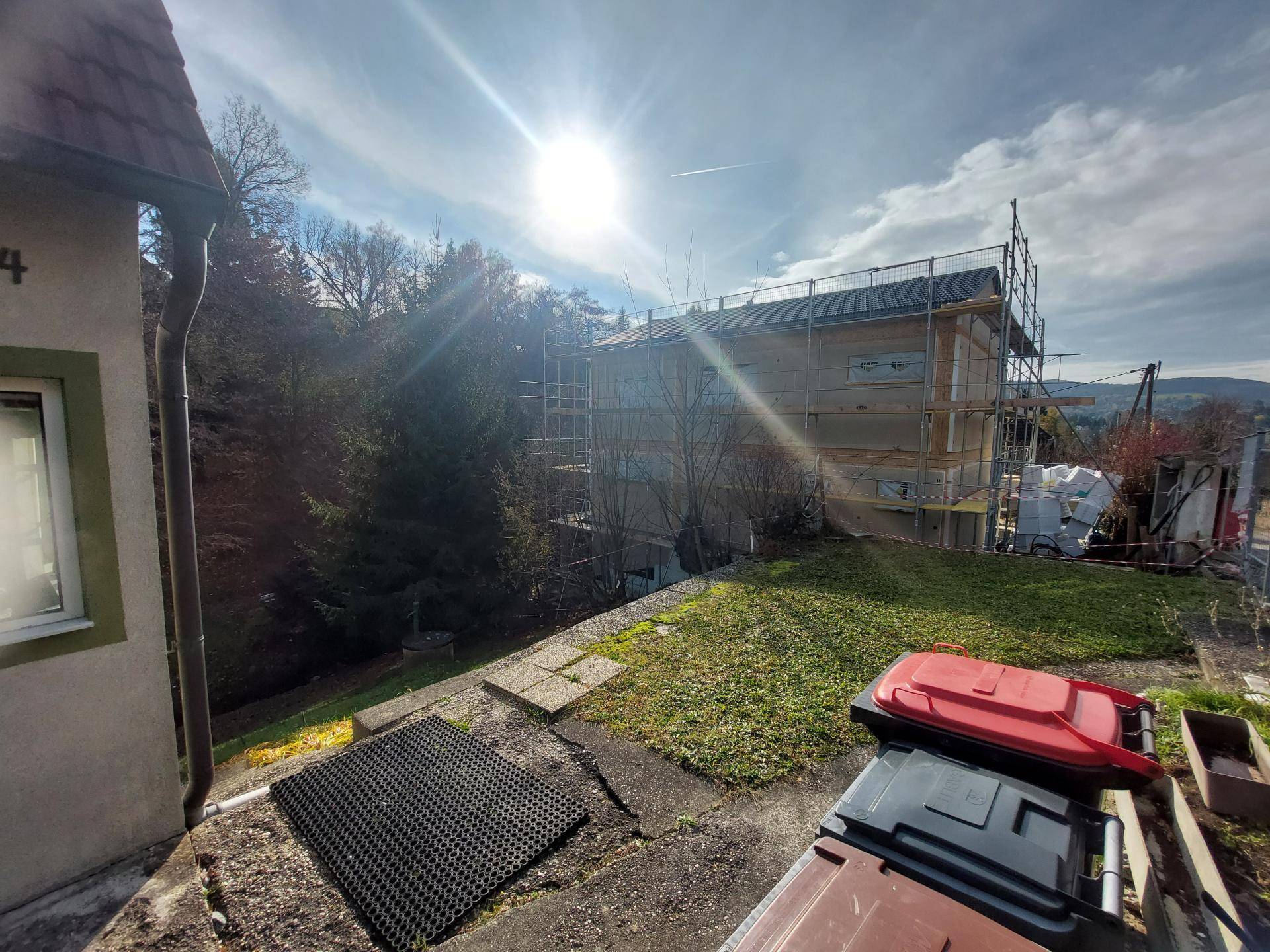Blick über den Garten auf ein benachbartes Gebäude im Bau unter strahlendem Sonnenschein.
