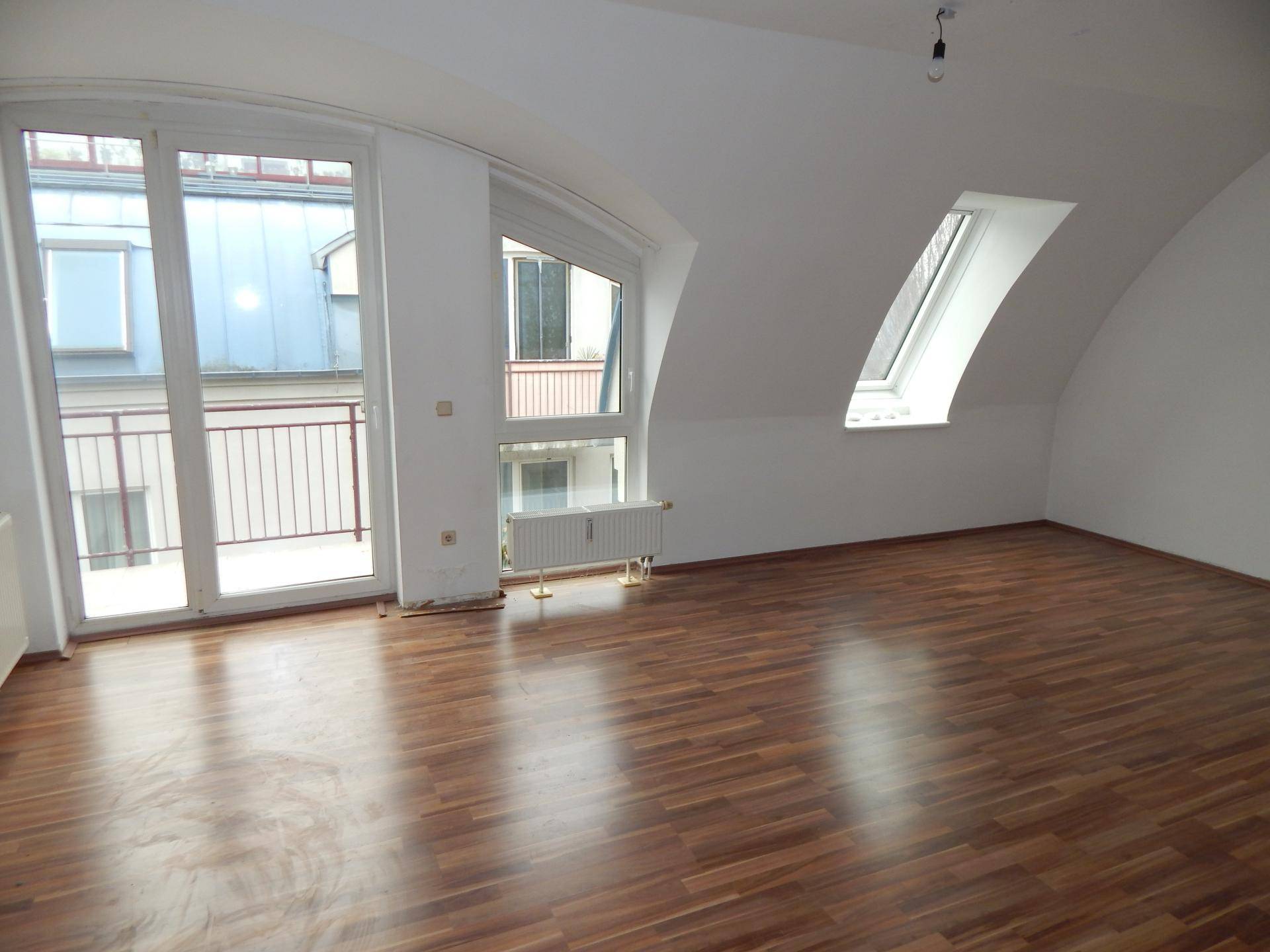 Heller Wohnraum im Dachgeschoss mit Laminatboden, Dachschrägen und Zugang zum Balkon.