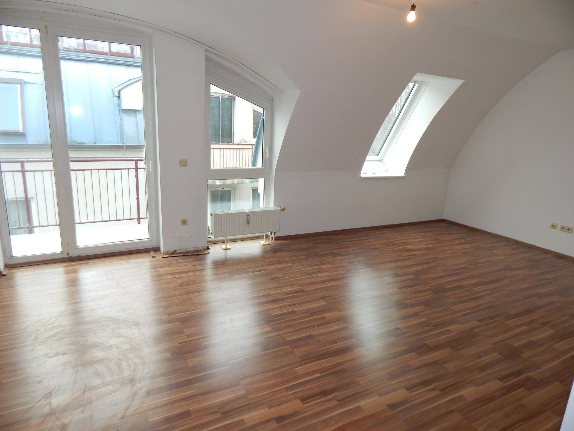 Geräumiger Wohnbereich im Dachgeschoss mit Laminatboden, Dachschrägen und Balkonzugang.