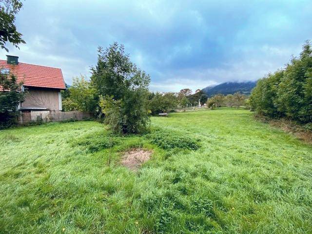 Offene Grünfläche mit Blick auf ein Haus mit rotem Dach und die umliegende Berglandschaft.