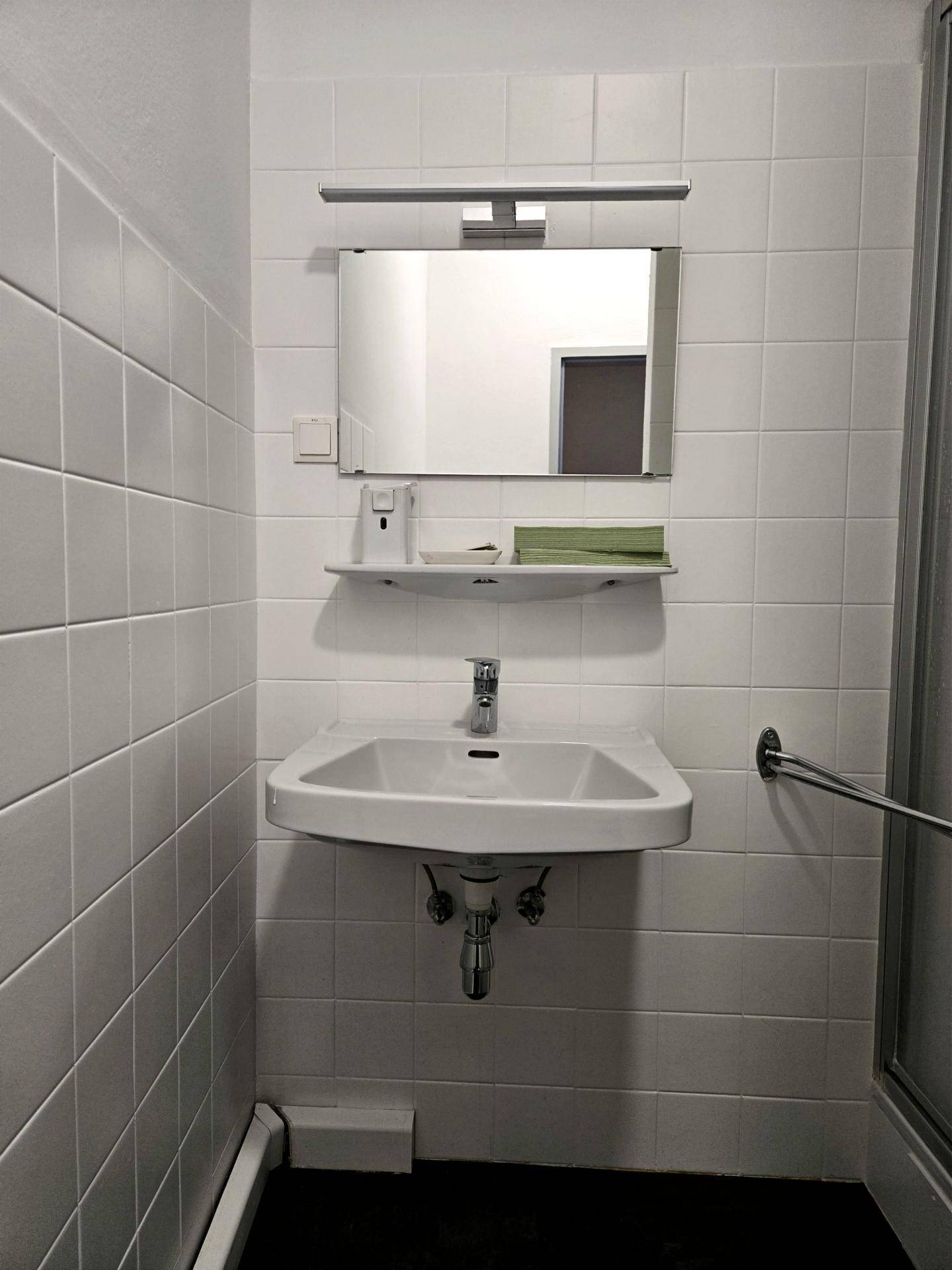 Badezimmer mit modernem Waschbecken, Spiegel und weißen Fliesen, das eine saubere Ästhetik bietet.