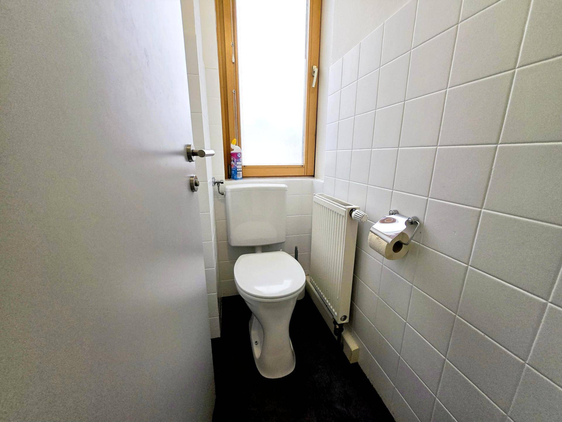 Separate Toilette mit WC, Heizkörper und Fenster, um natürliche Belüftung und Licht zu gewährleisten.