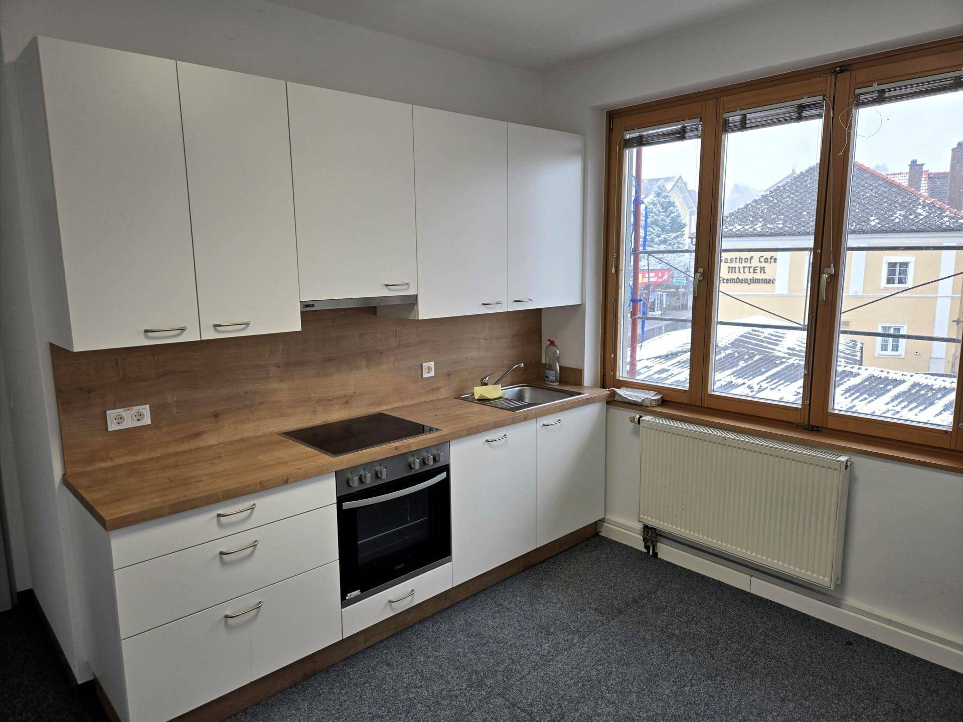 Detailansicht der modernen Küchenzeile mit weißen Schränken, Holzarbeitsplatte und integrierten Geräten.