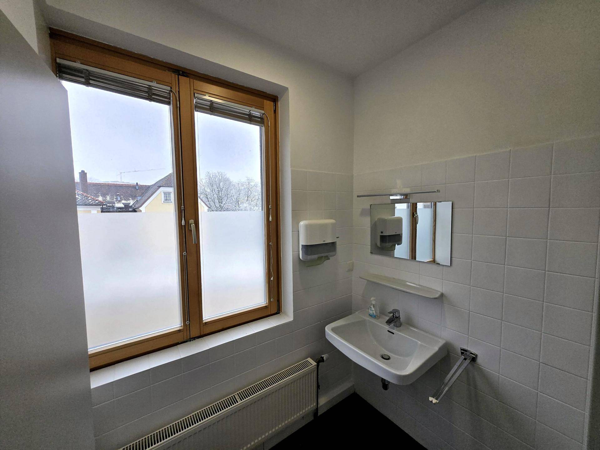 Badezimmer mit Waschbecken, weißen Fliesen und einem Fenster, das für natürliche Belüftung sorgt.