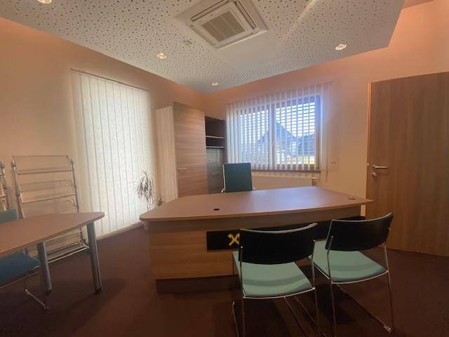 Helles Büro mit großem Schreibtisch, Bürostühlen und einem Fenster mit Jalousien, ausgestattet mit Teppichboden.