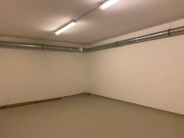 Leerer Kellerraum mit sichtbaren Lüftungsrohren und einem hellen Boden, ideal als Lagerfläche.