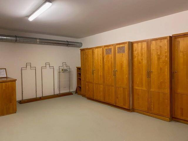 Kellerraum mit Holzschränken und sichtbaren Lüftungsrohren, der als Archiv oder Lagerraum dient.